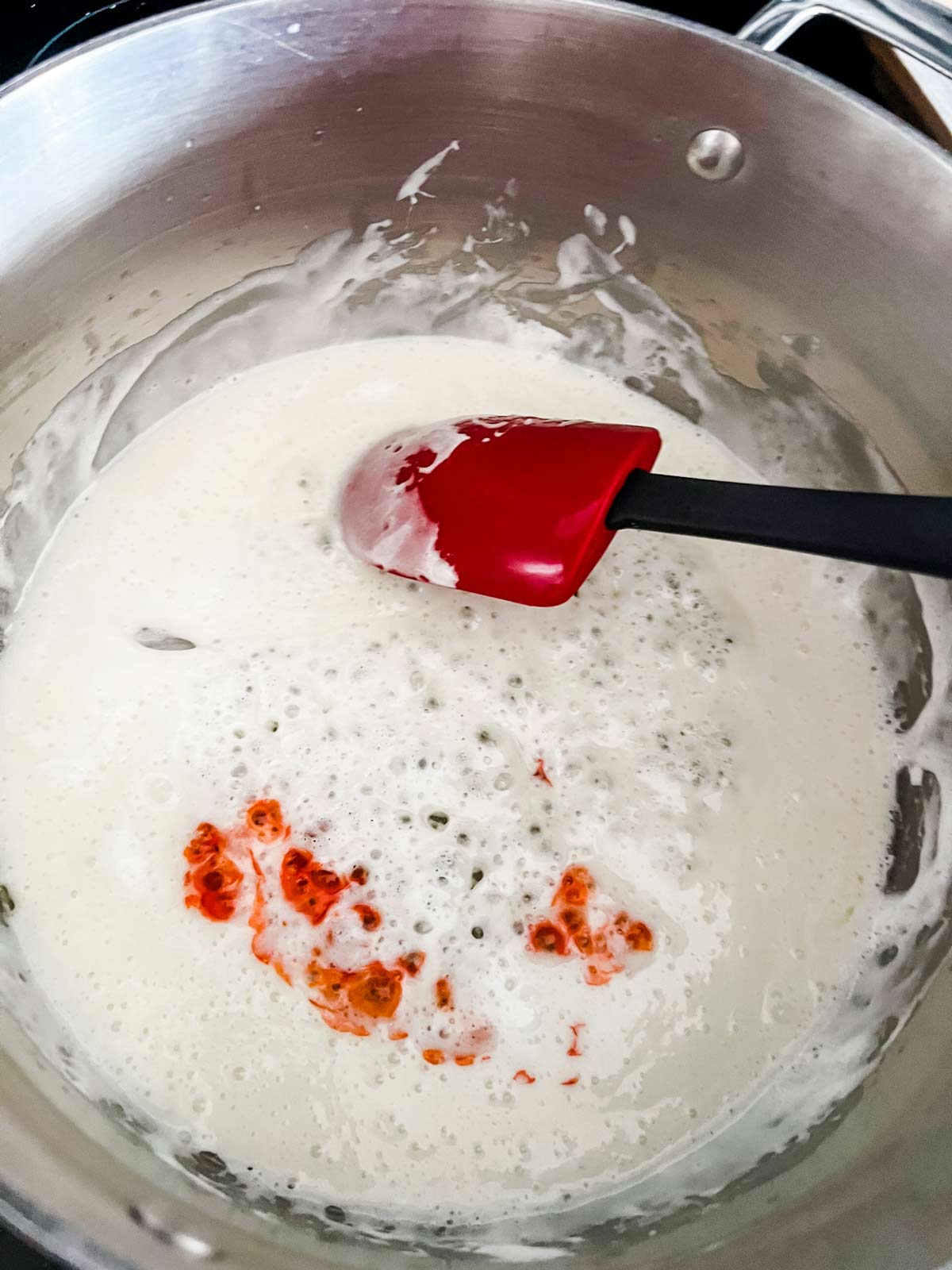 Orange food coloring added to melted marshmallows in a pot.