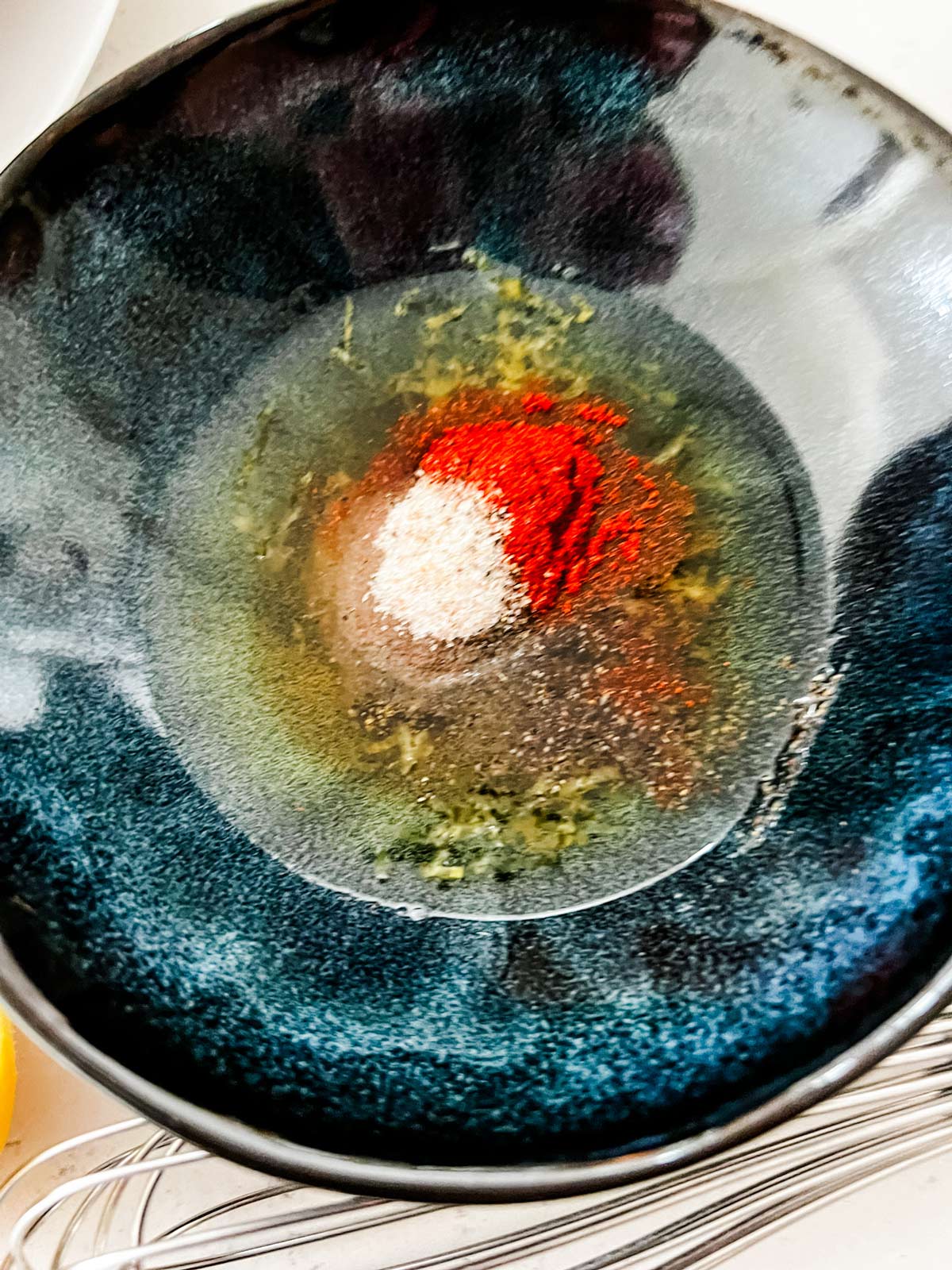 Overhead photo of oil, lemon zest, and seasonings in a small bowl.