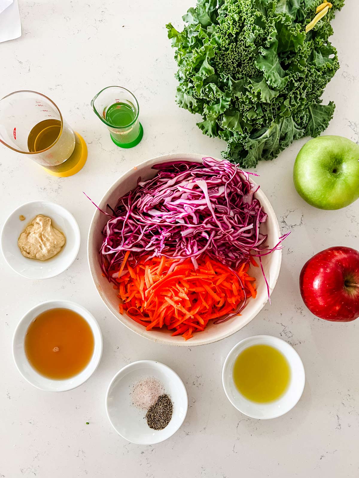 Overhead photo of kale, apples, carrot, cabbage, and salad dressing ingredients.