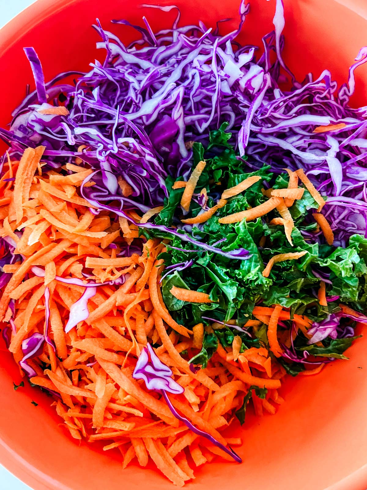 Massaged kale, carrot, and cabbage in an orange bowl.