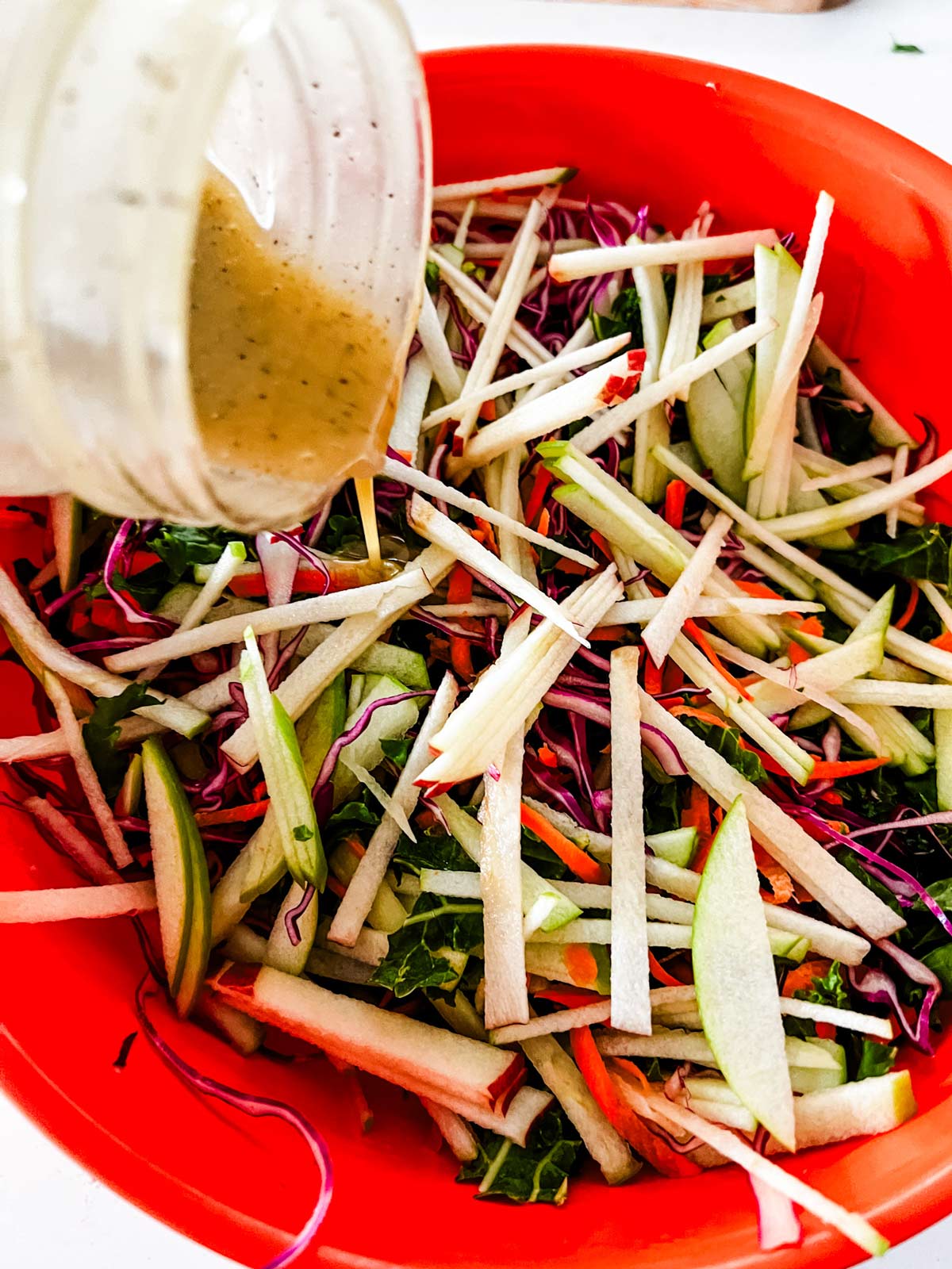 Overhead photo of kale apple slaw in a bowl with dressing being poured on it.