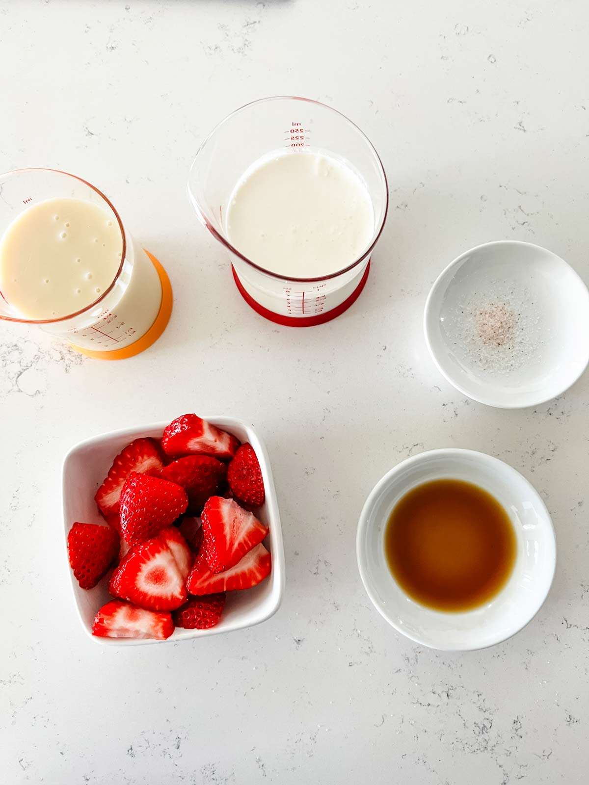 Overhead photo of sliced strawberries, condensed milk, cream, salt, and vanilla.