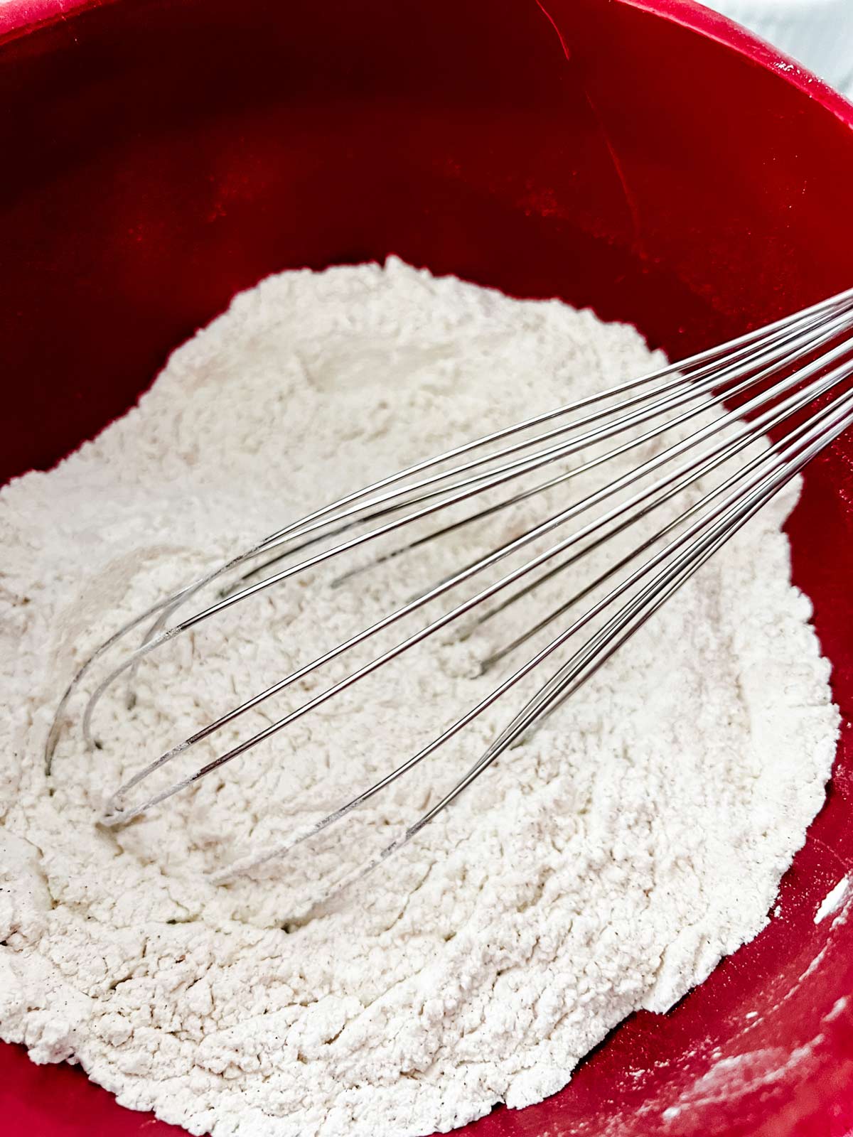 Dry ingredients for cookies being whisked together in a red bowl.