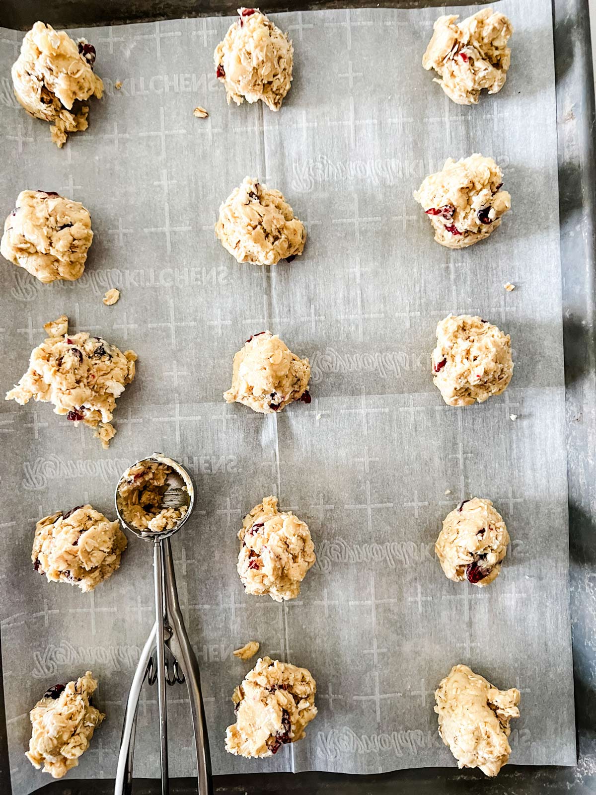 A cookie scoop on a parchment lined baking sheet with scooped out cookies.