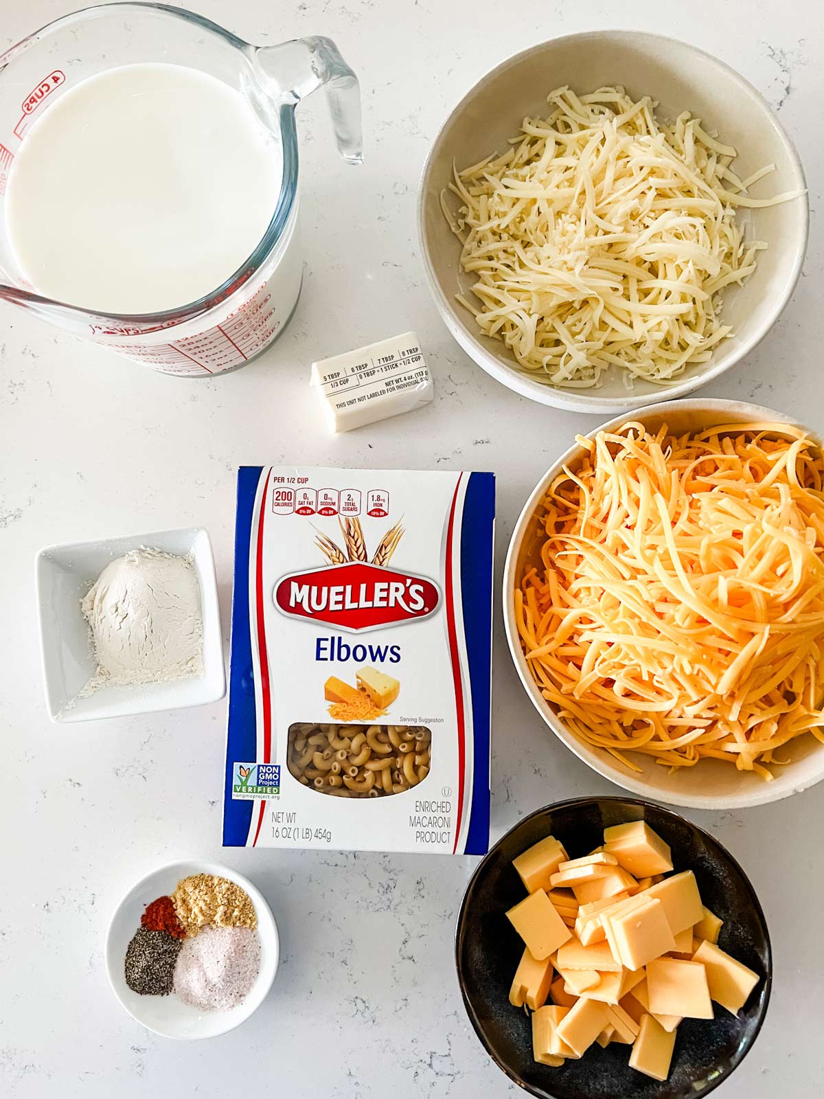 Overhead photo of three cheeses, elbow noodles, milk, four, butter, and seasonings.