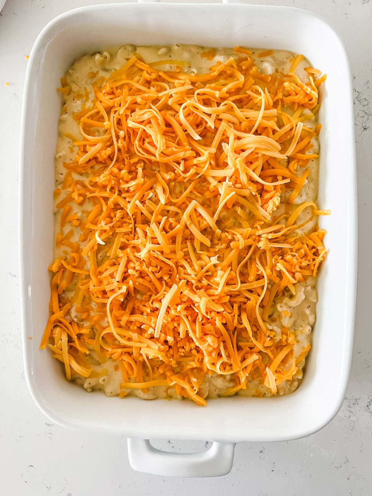 Macaroni and cheese with shredded cheese on top in a white casserole dish.