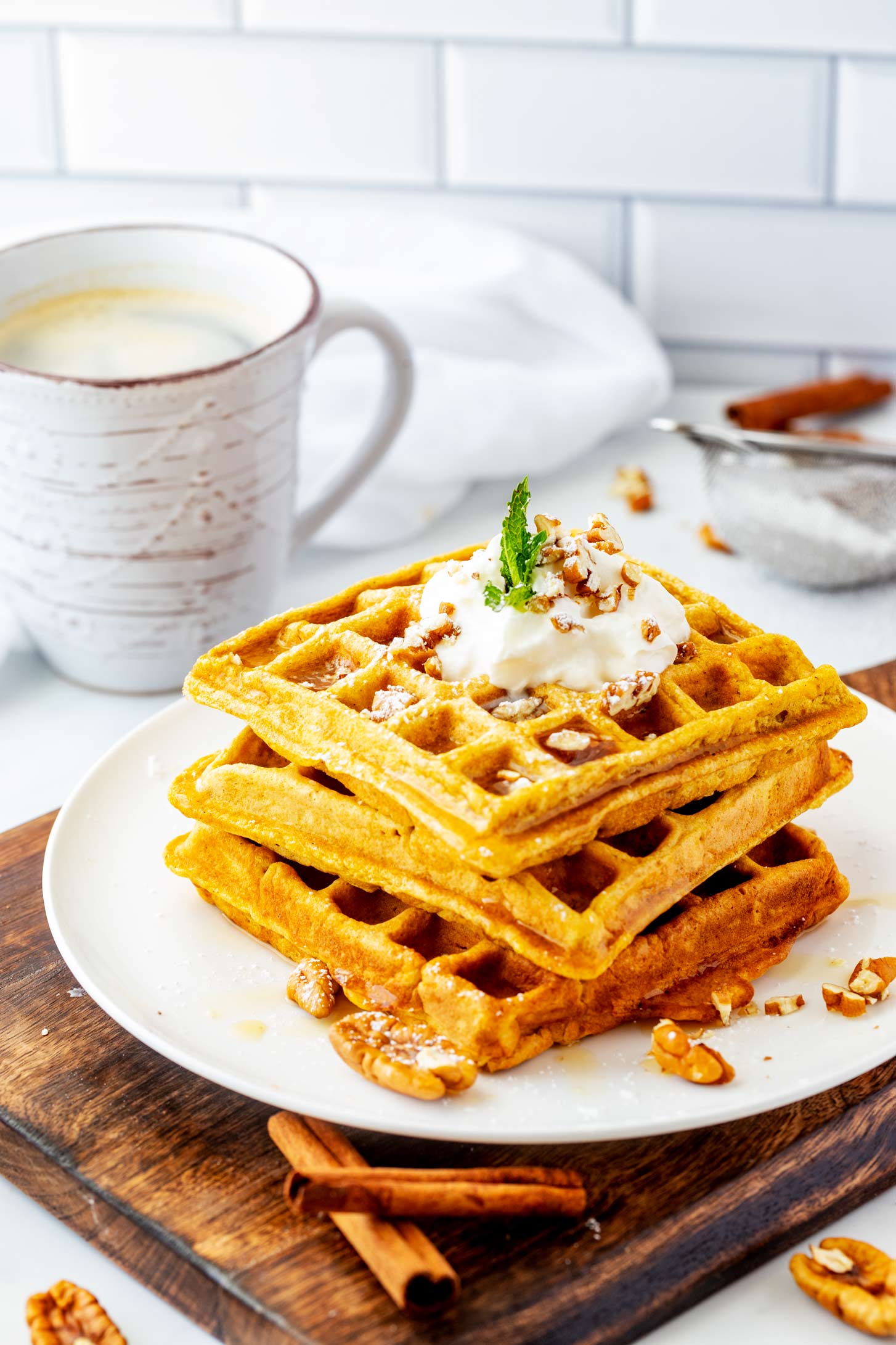 Side photo of three stacked pumpkin waffles garnished with pecans, syrup, and whipped cream.