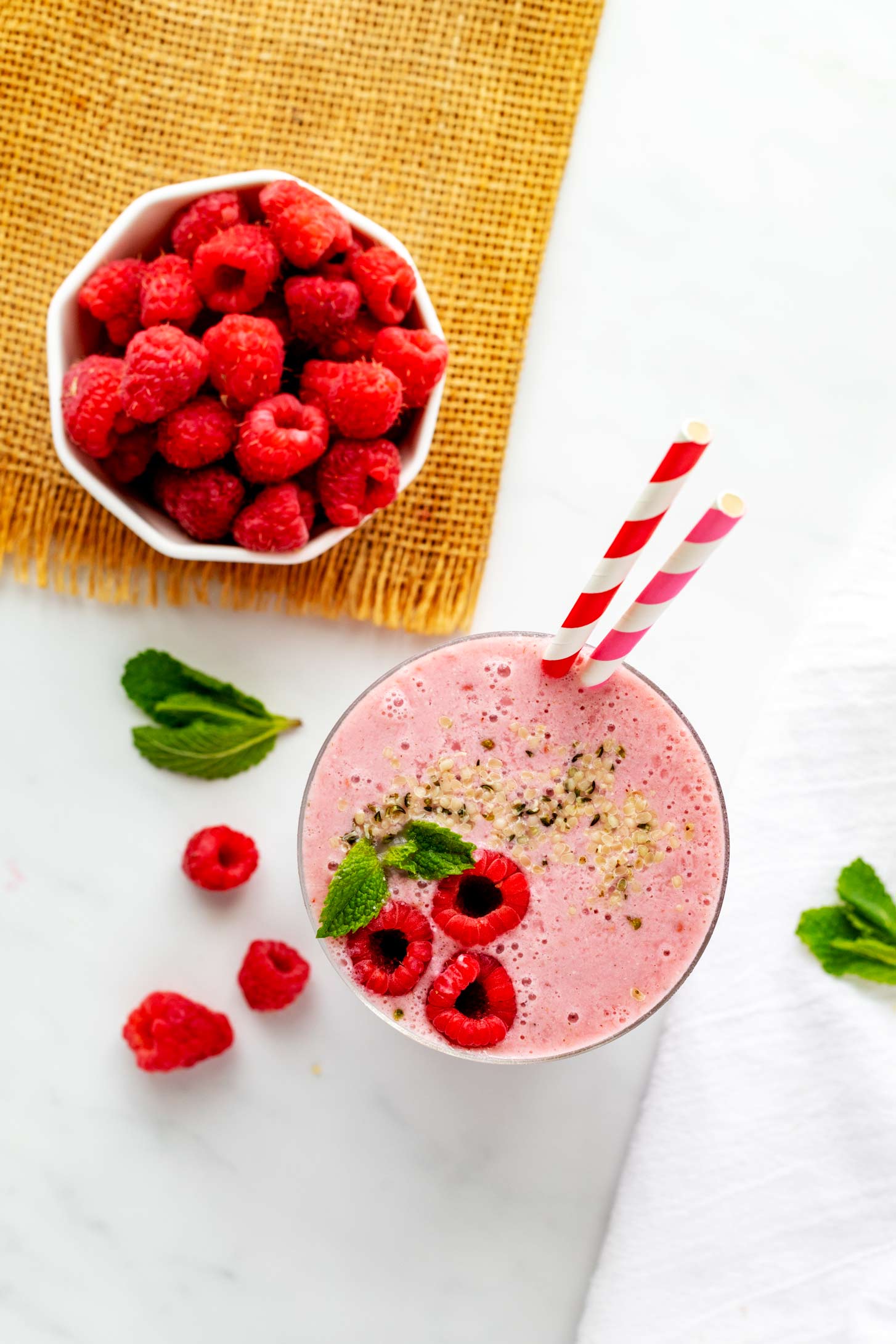 Overhead photo of a raspberry smoothie on a white countertop sitting next to a small bowl of raspberries.
