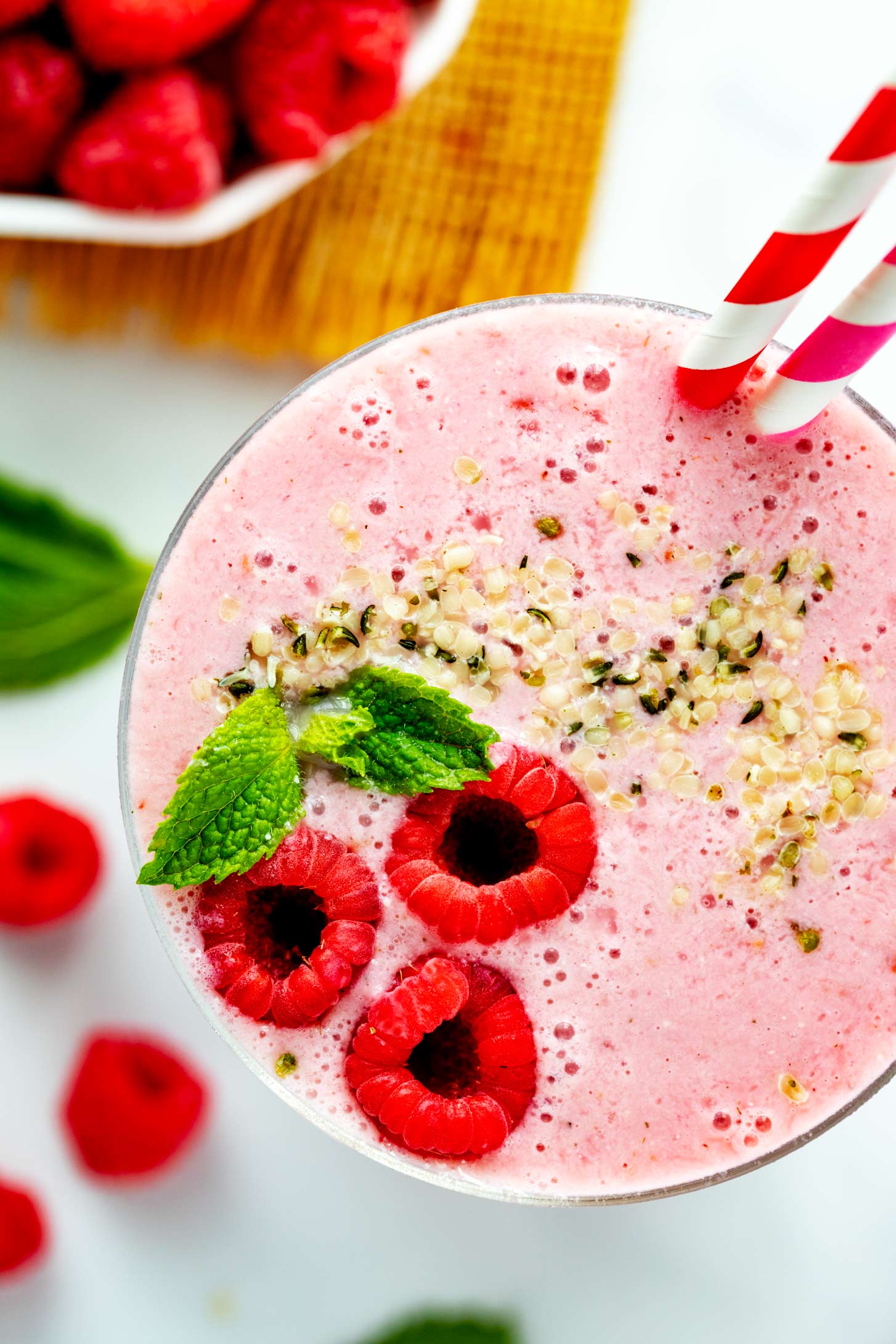 Overhead close up photo of a raspberry smoothie garnished with fresh raspberries, mint, and hemp seeds.