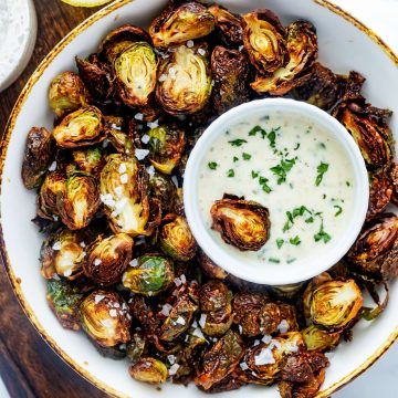 Close up photo of crispy air fryer brussels sprouts in a bowl with a dipping sauce.