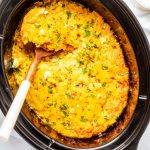 Square overhead photo of crockpot corn casserole in a crockpot with a spoon dipping out a portion.