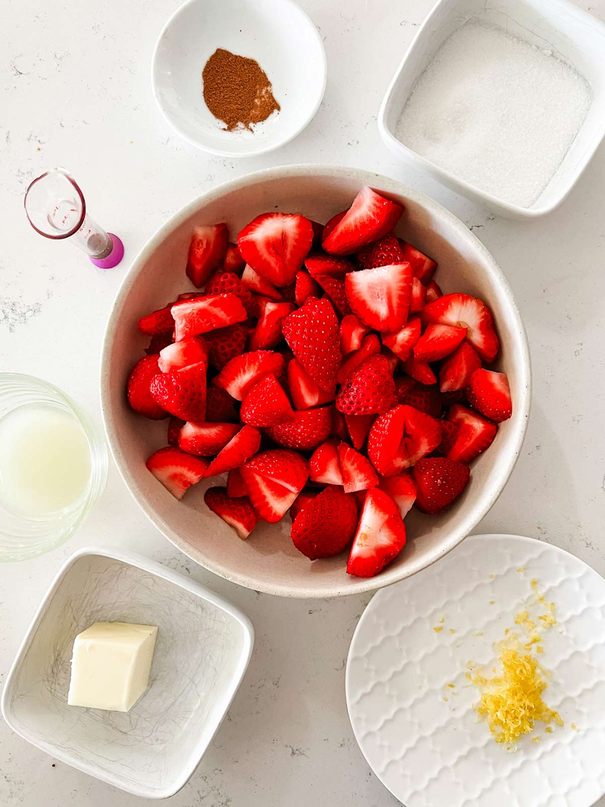 Overhead photo of strawberries, sugar, cinnamon, vanilla, lemon juice, zest, and butter.