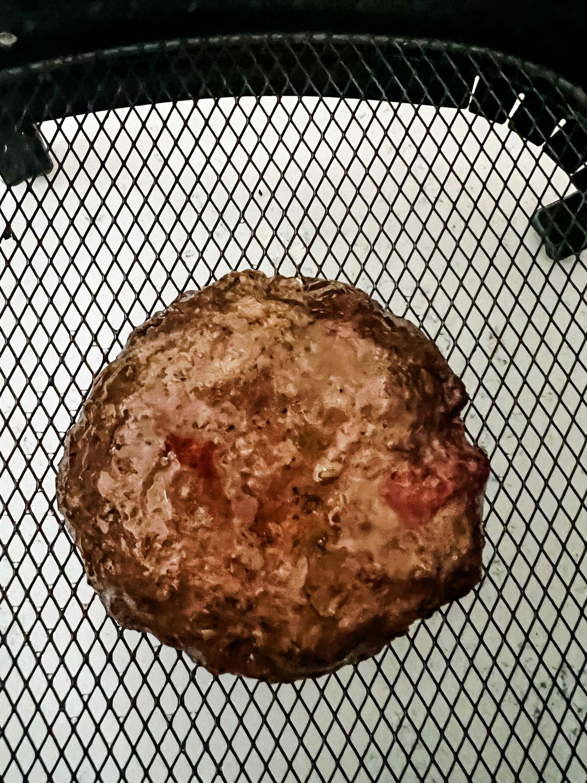 A burger patty in an air fryer basket.