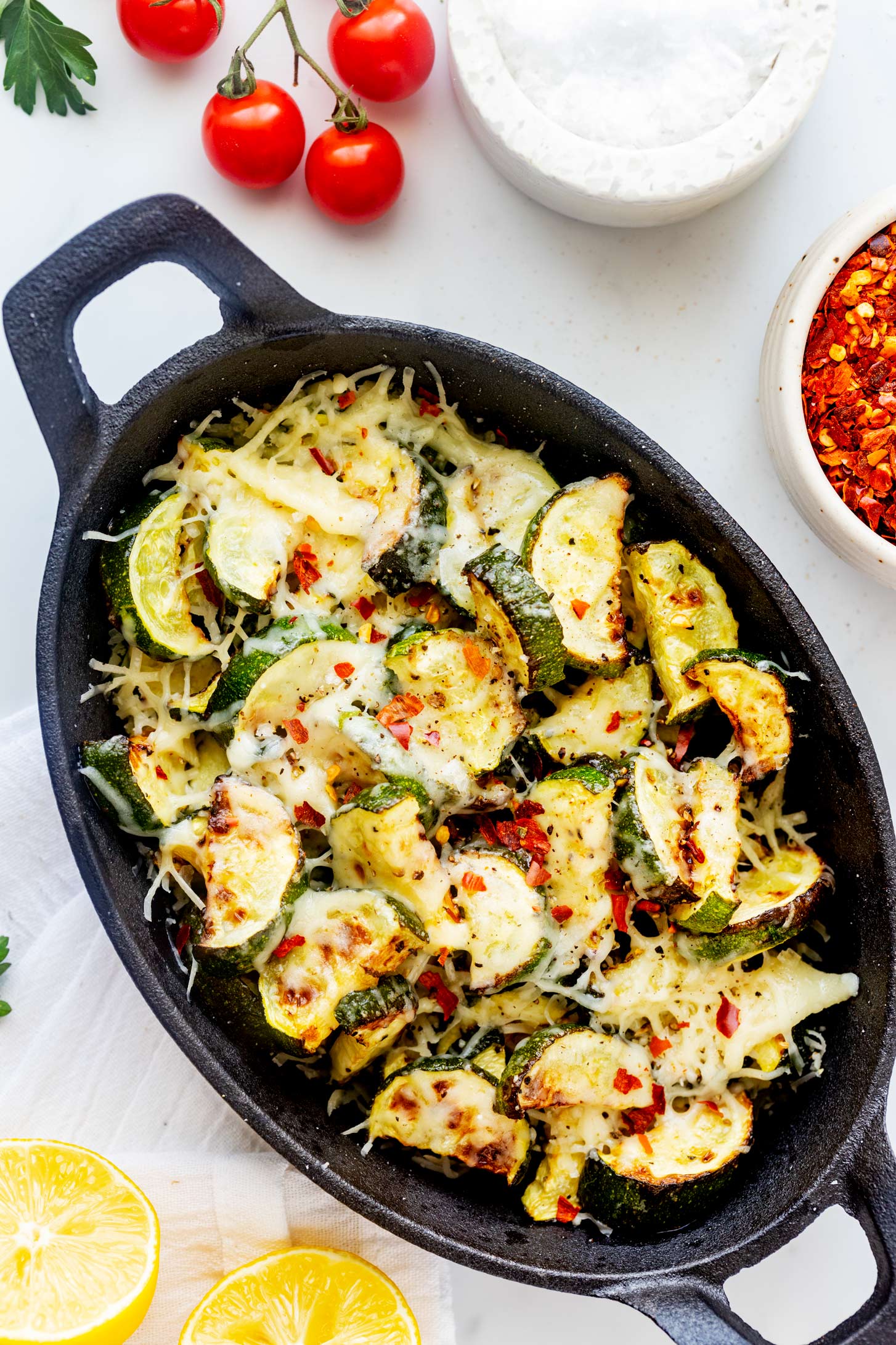 Overhead photo of air fryer zucchini in a black cast iron serving dish garnished with red pepper flakes.