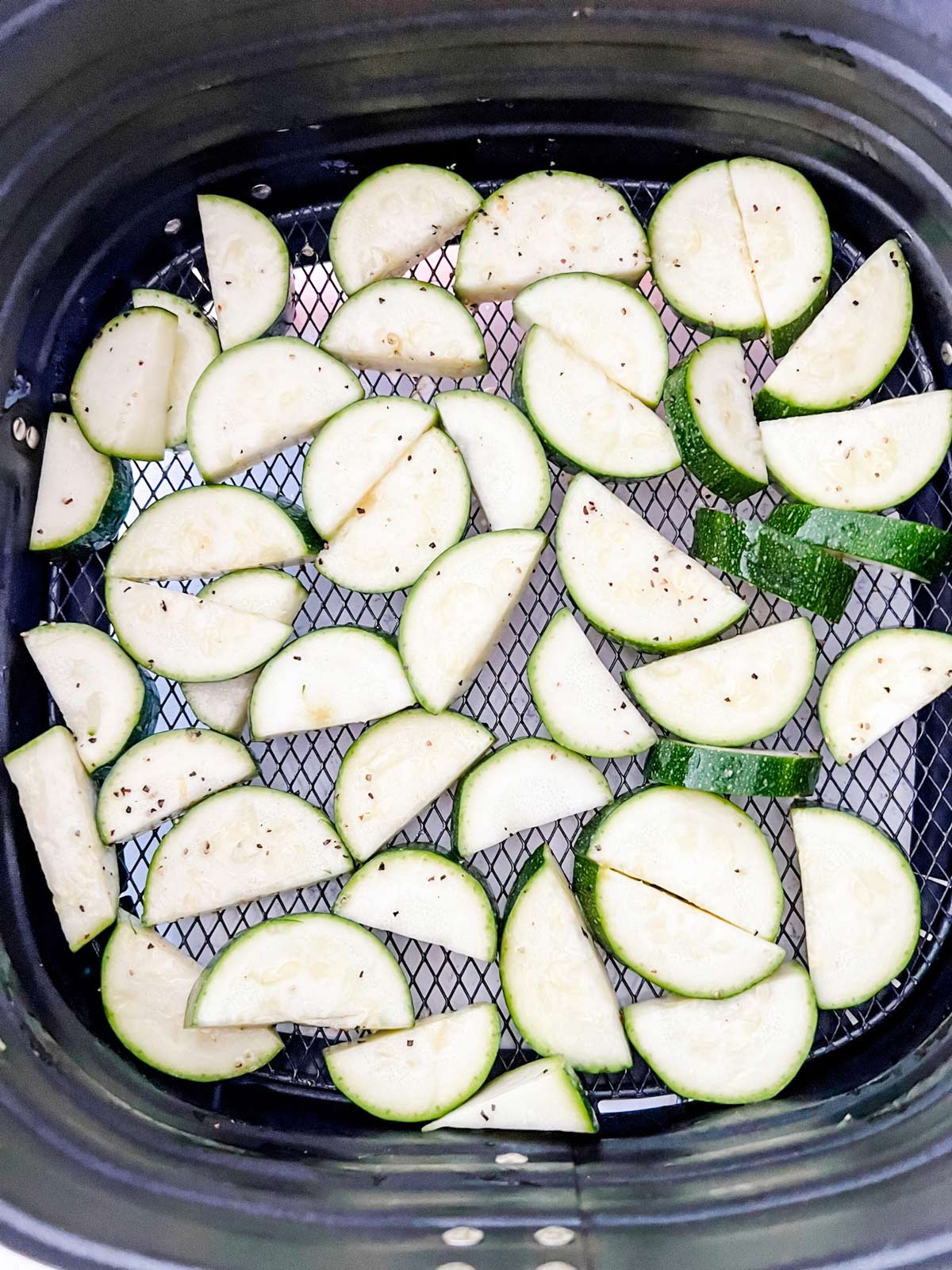 Sliced zucchini in the basket of an air fryer.
