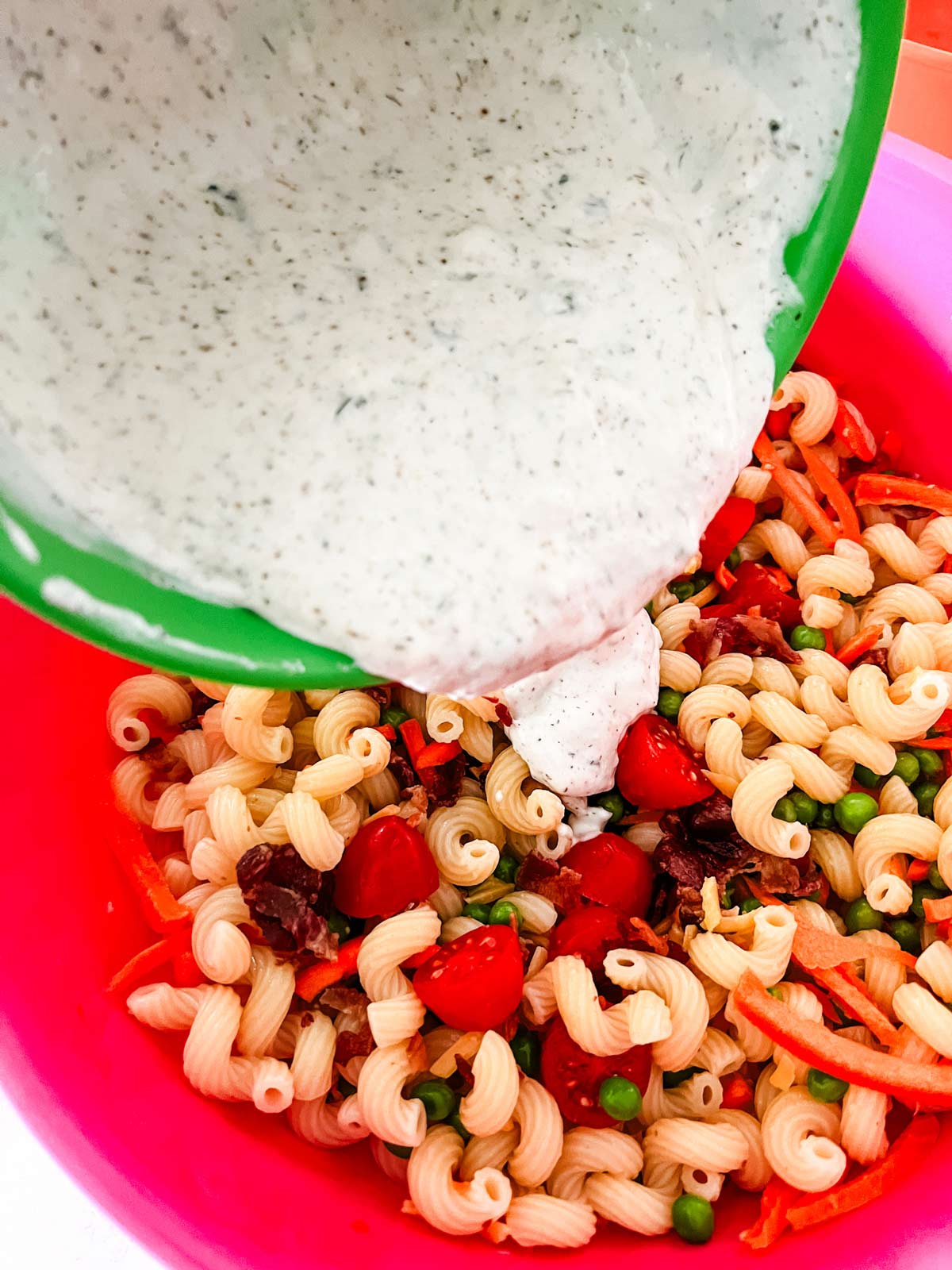 Bacon ranch pasta salad with ranch dressing being poured over it.