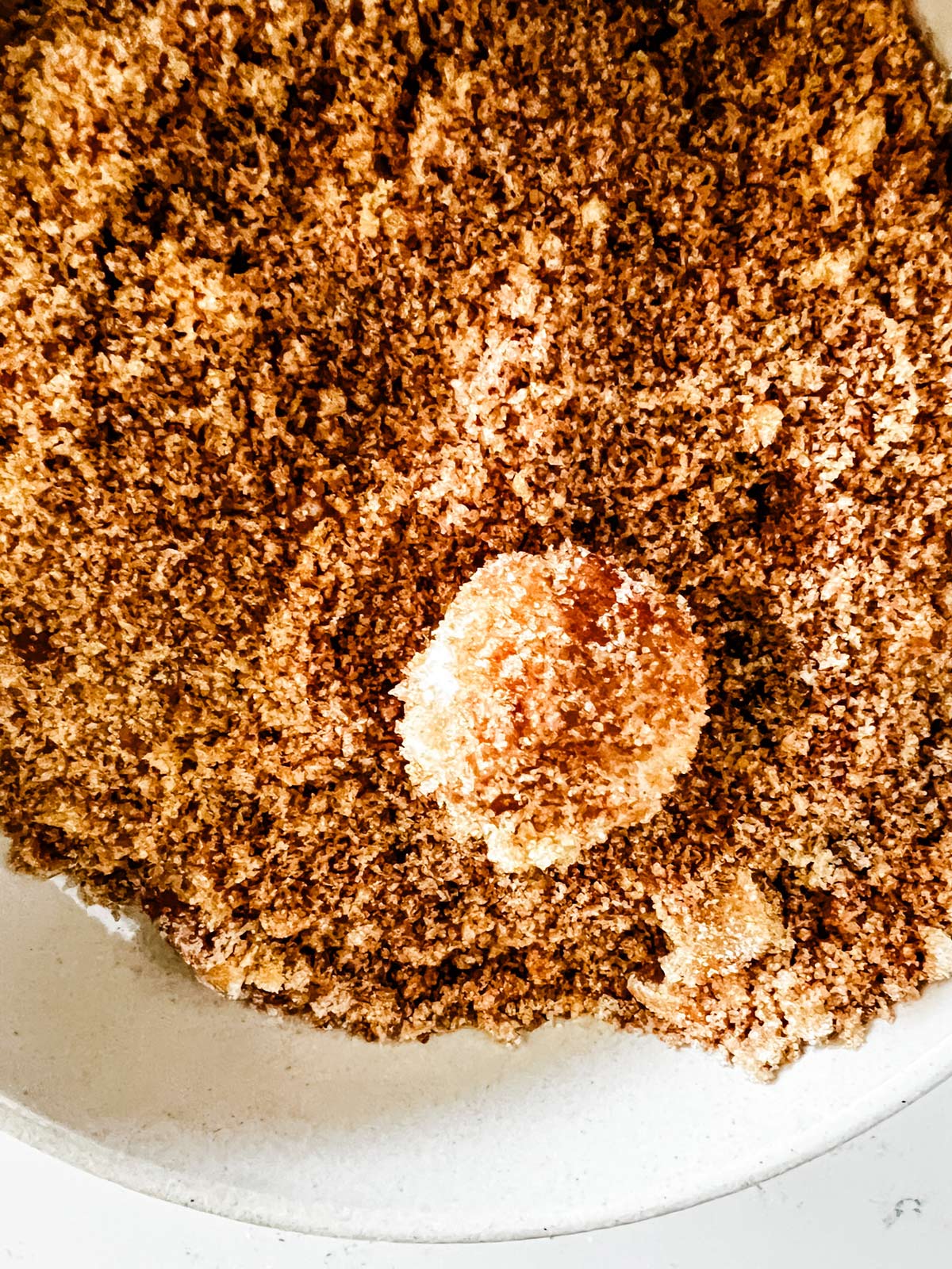 Monkey bread dough being tossed in a bowl of cinnamon sugar.