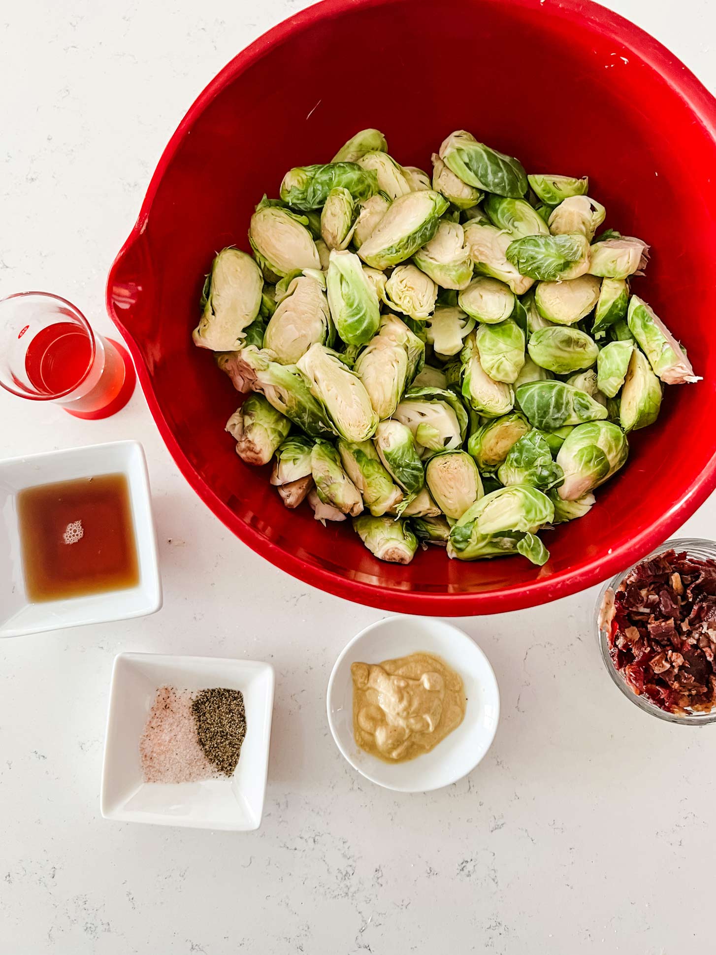 Overhead photo of brussels sprouts, bacon, mustard, salt, pepper, maple syrup, and oil.