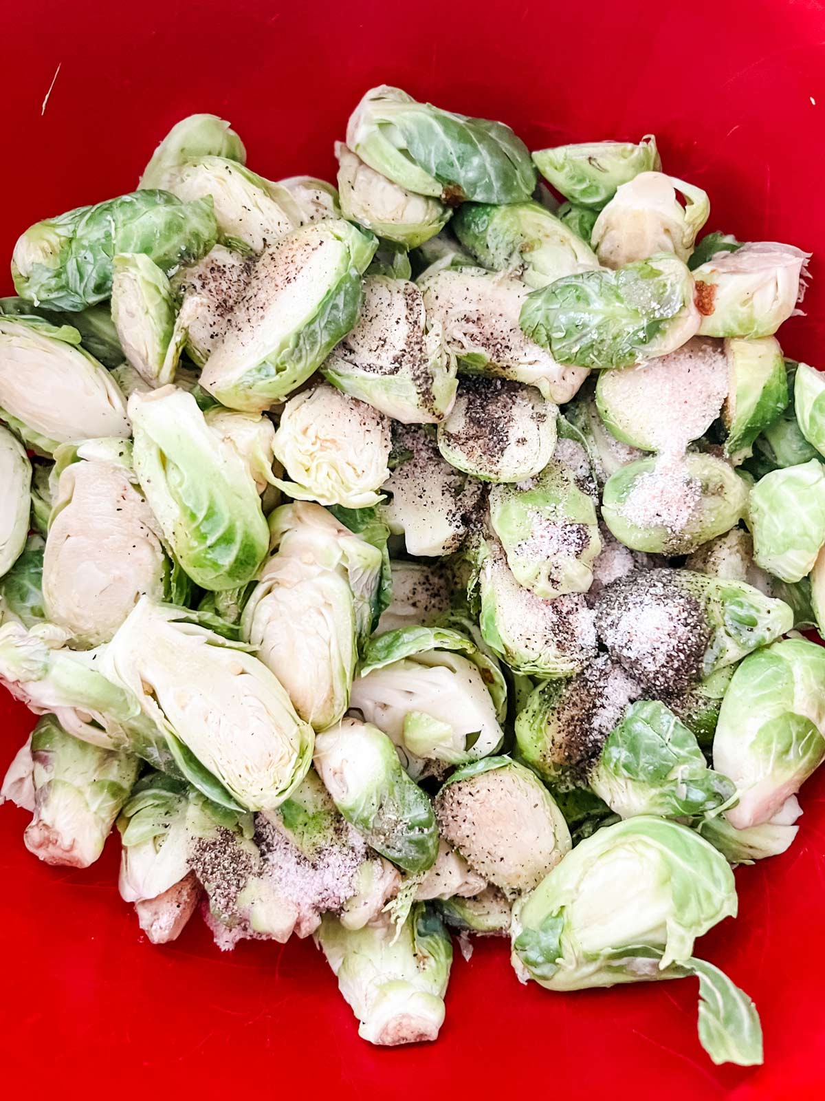 Brussels sprouts in a red bowl with seasonings on top.