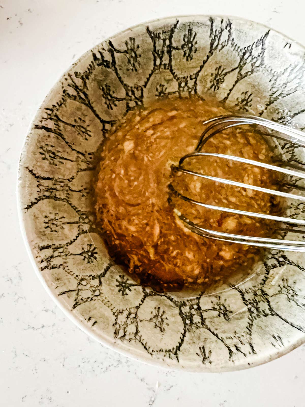 Oil, maple syrup, dijon mustard, and seasonings being whisked together in a small bowl.