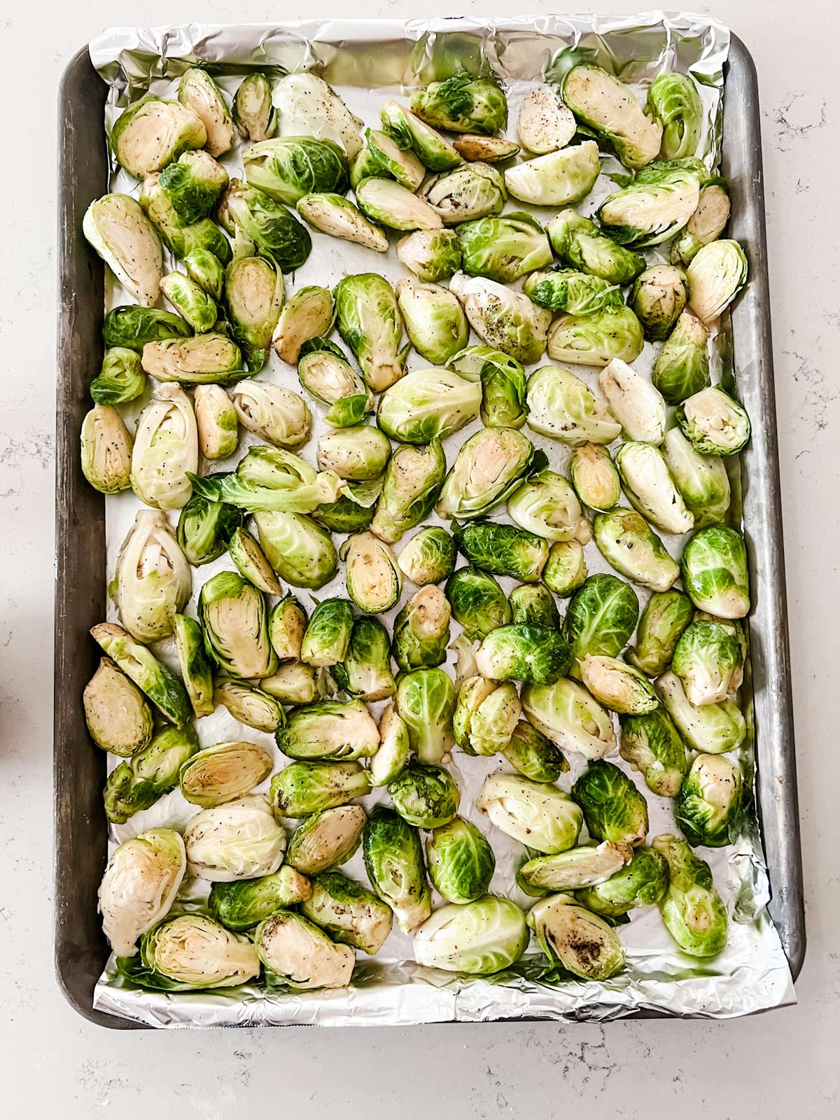 Photo of a foil lined baking sheet with seasoned Brussels sprouts.
