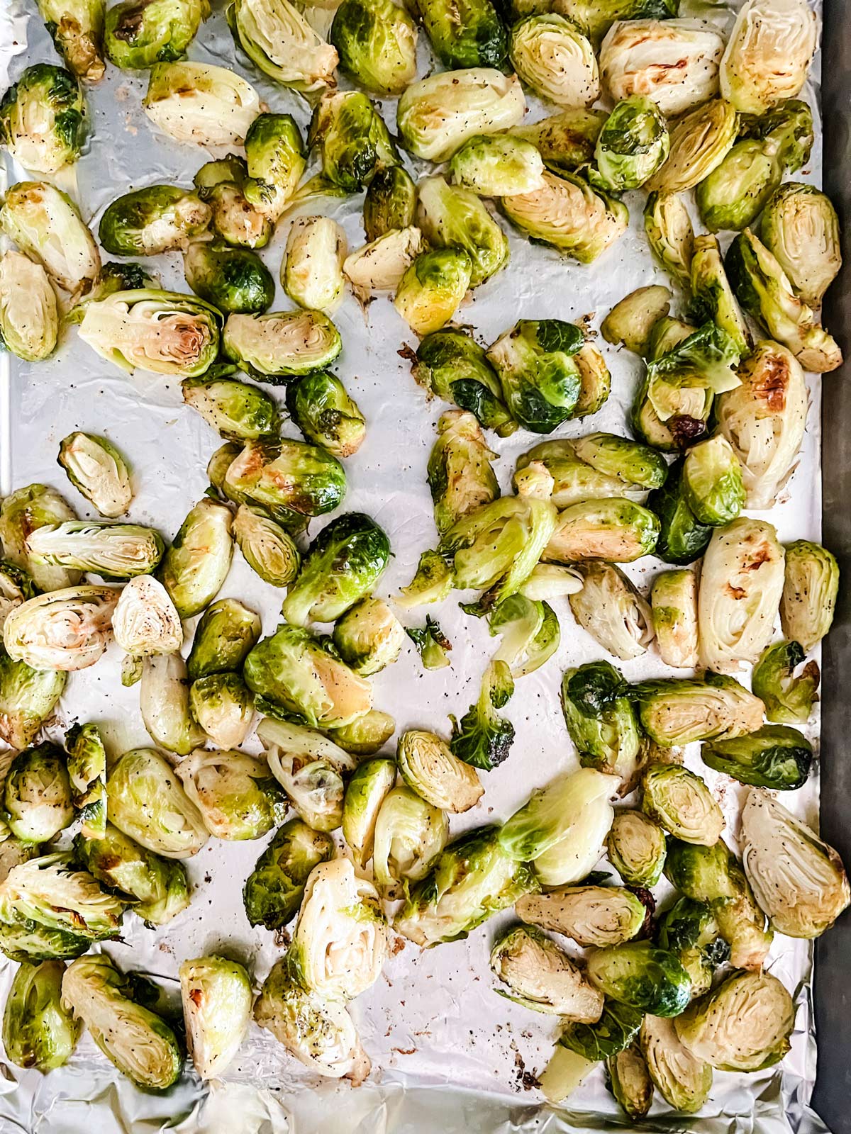 Partially roasted Brussels sprouts on a foil lined baking sheet.