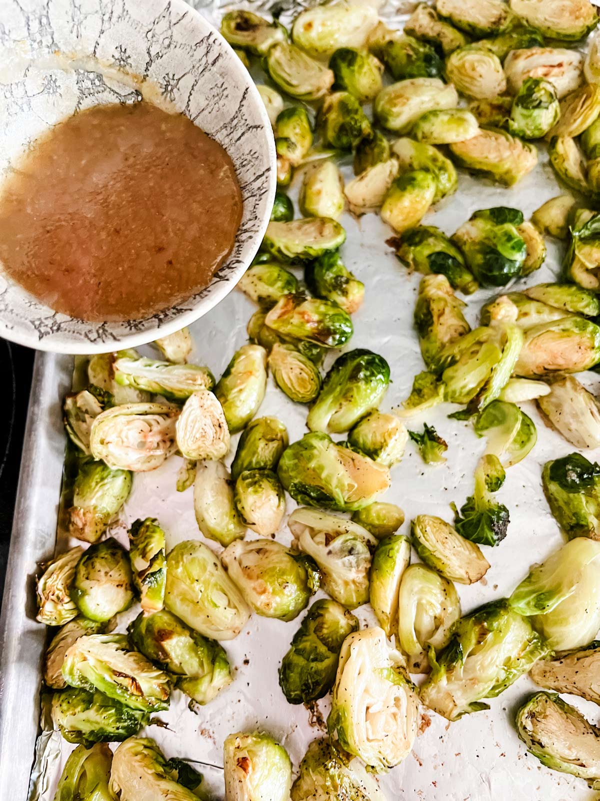 A maple glazede being poured over partially roasted Brussels sprouts.