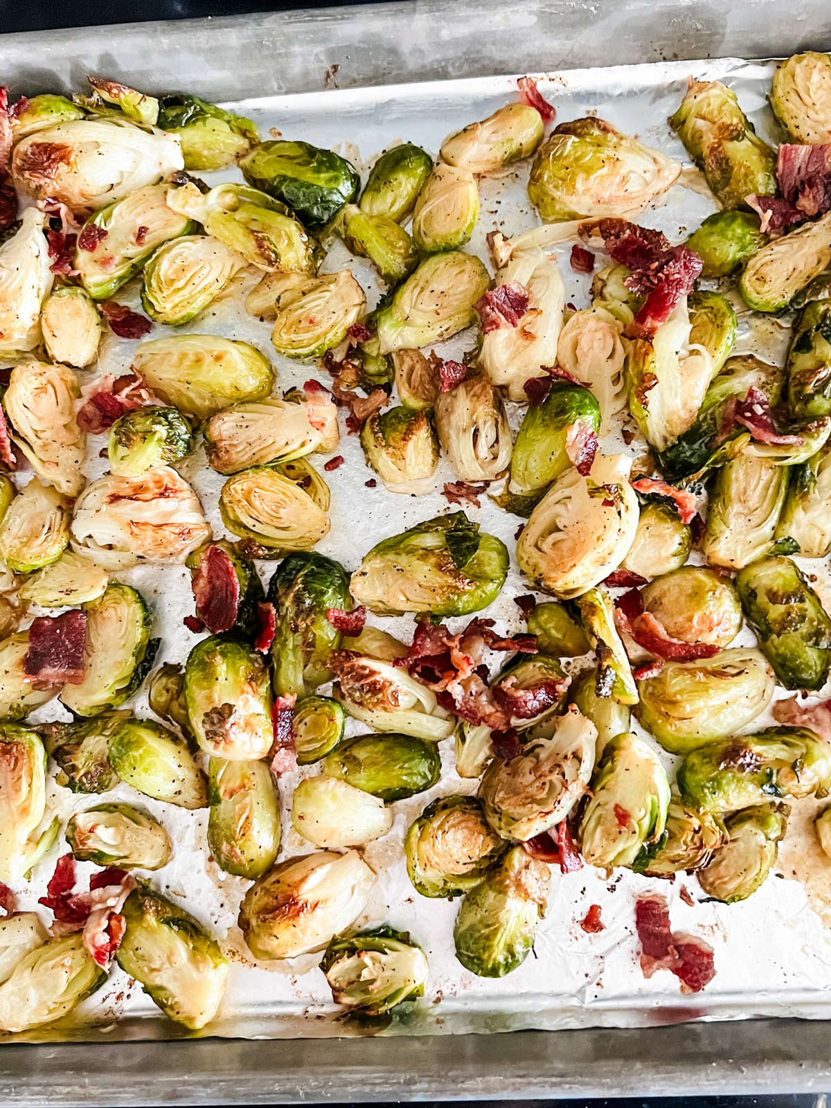 Bacon scattered over Brussels sprouts on a foil lined baking sheet.