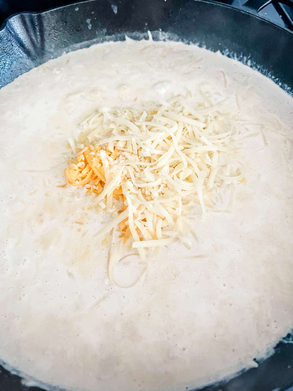 A cream sauce with shredded cheese on top in a cast iron skillet.