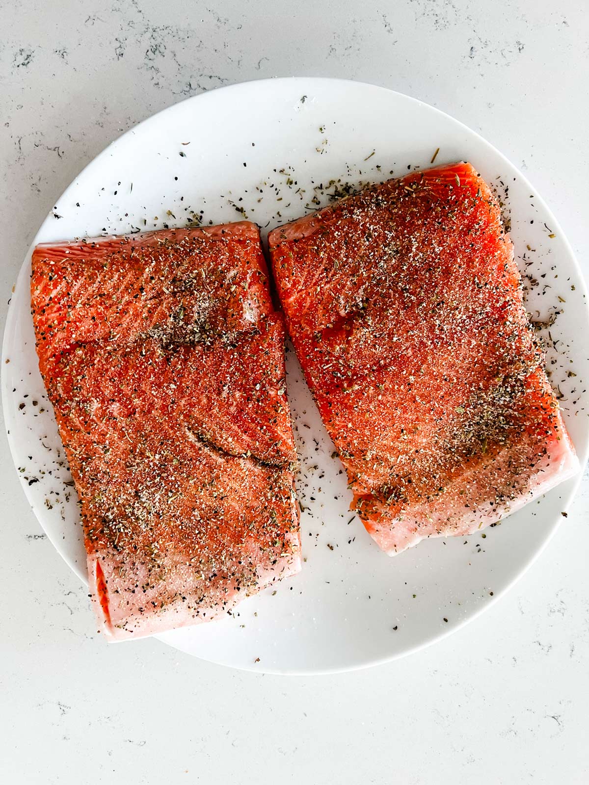 Seasoned salmon filets on a white plate.