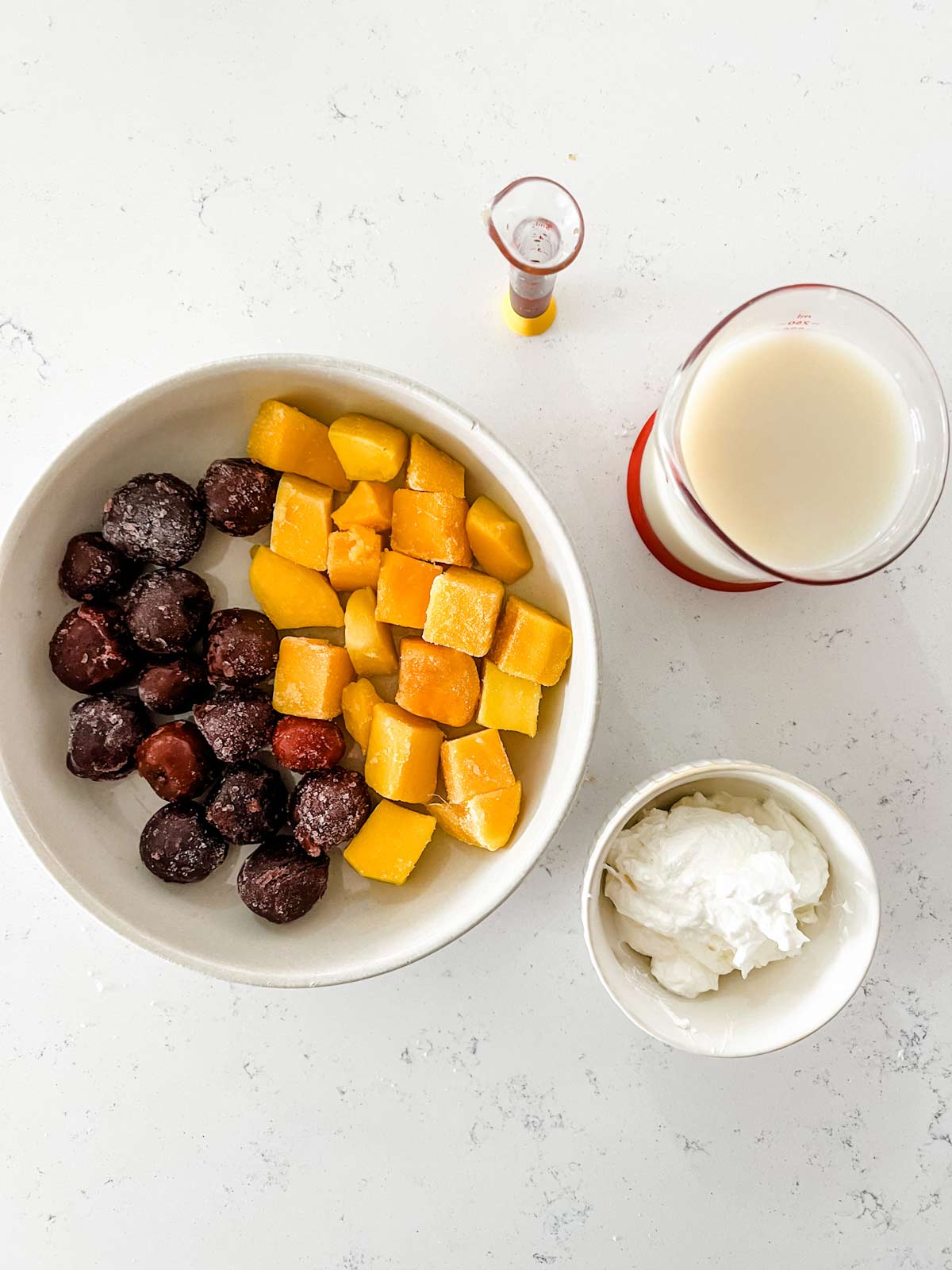 Overhead photo of cherries, mango chunks, oat milk, yogurt, and vanilla in prep bowls.