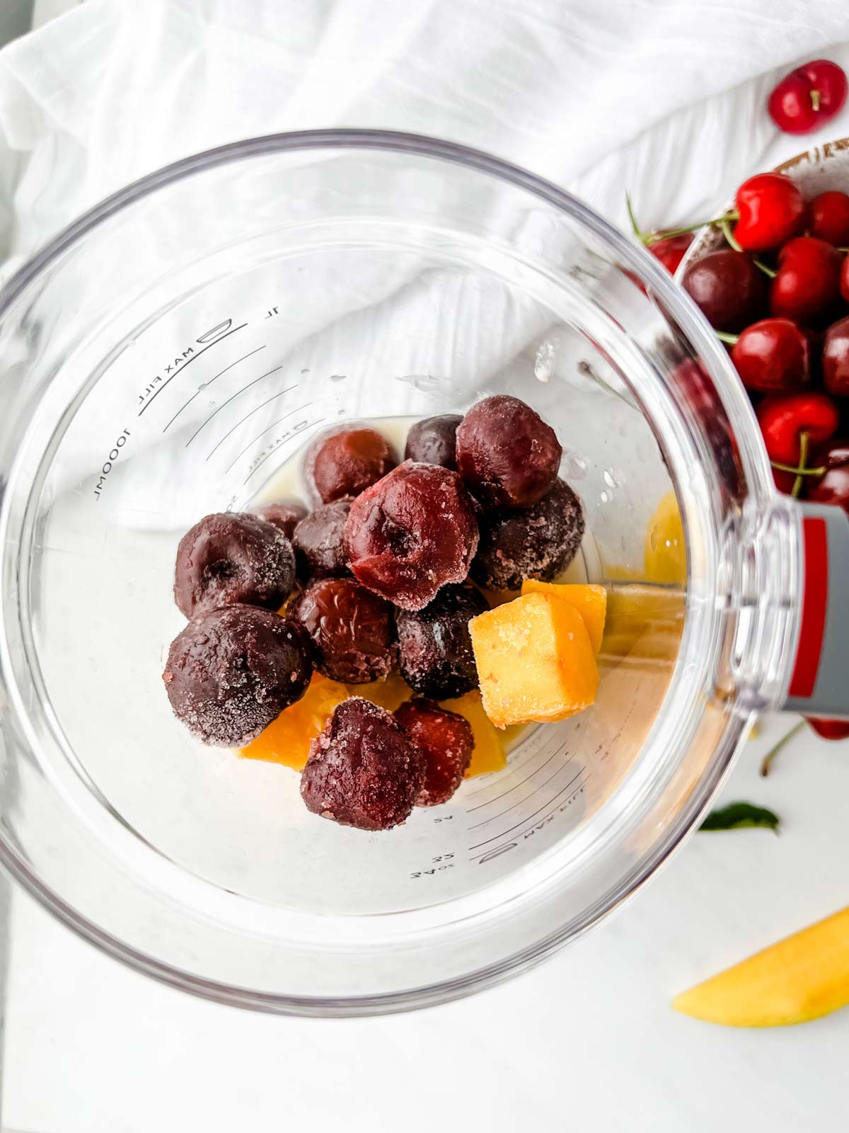 A blender with the ingredients for a cherry mango smoothie in it ready to process.
