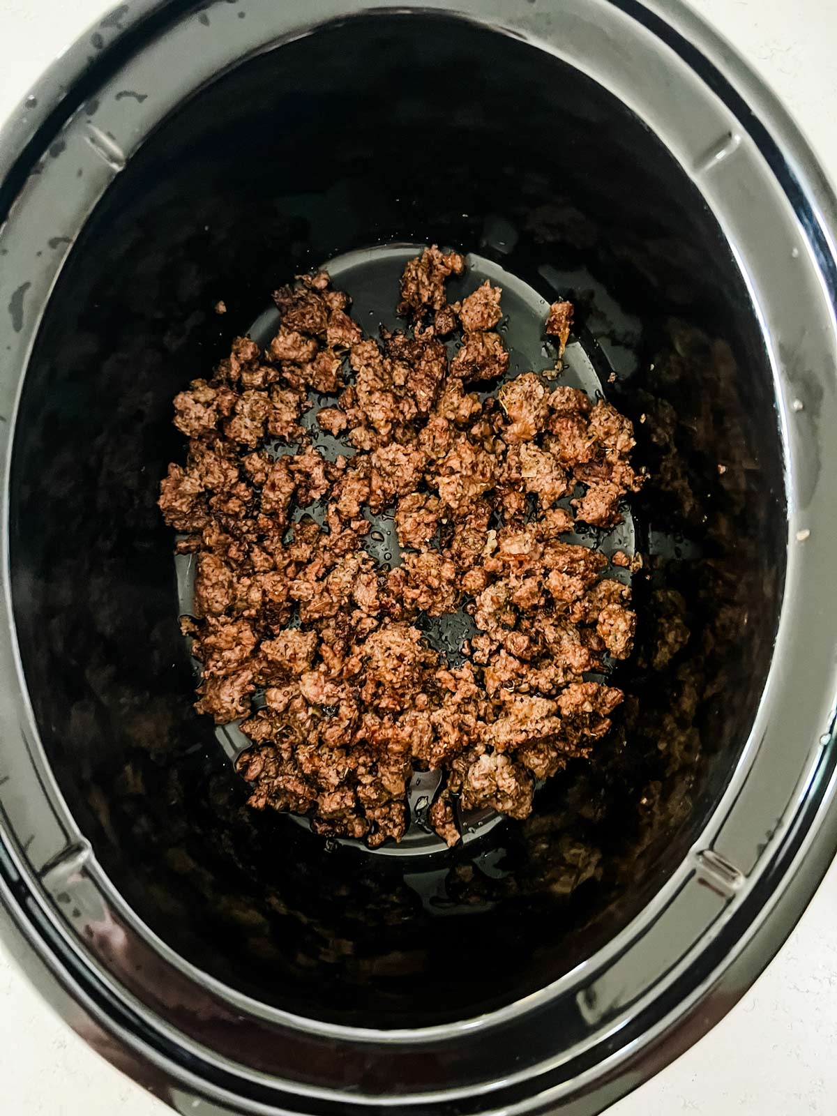 Photo of ground beef in the bottom of a slow cooker.