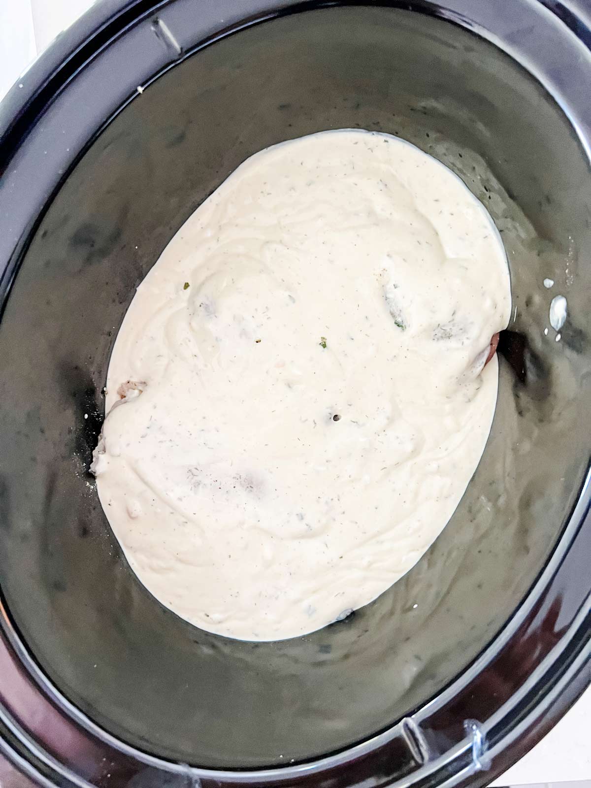 Overhead photo of chicken in a slow cooker covered in a creamy ranch sauce.