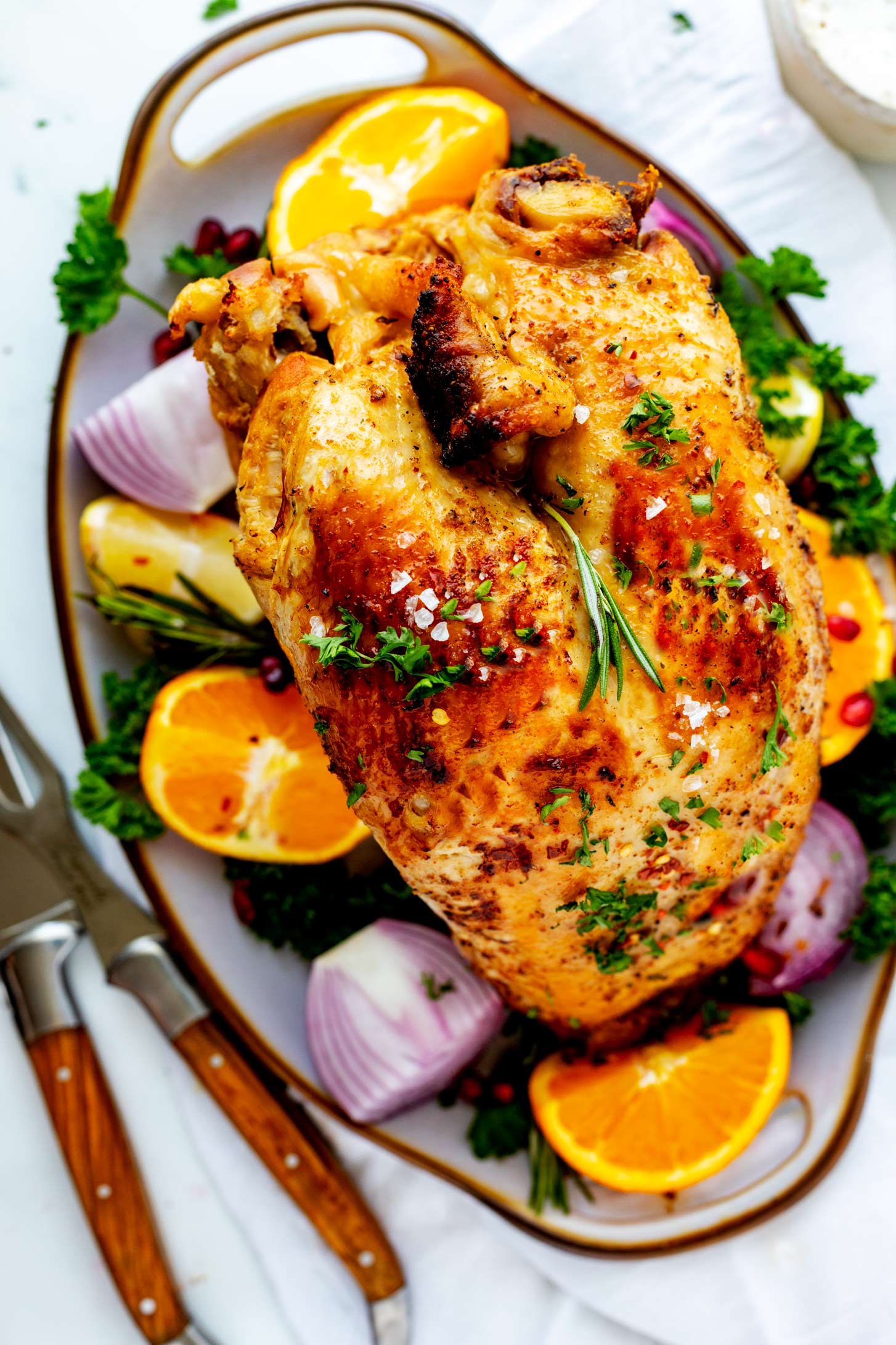 Overhead photo of a crockpot turkey breast on a serving platter surrounded by onion, parsley, lemon, and orange.