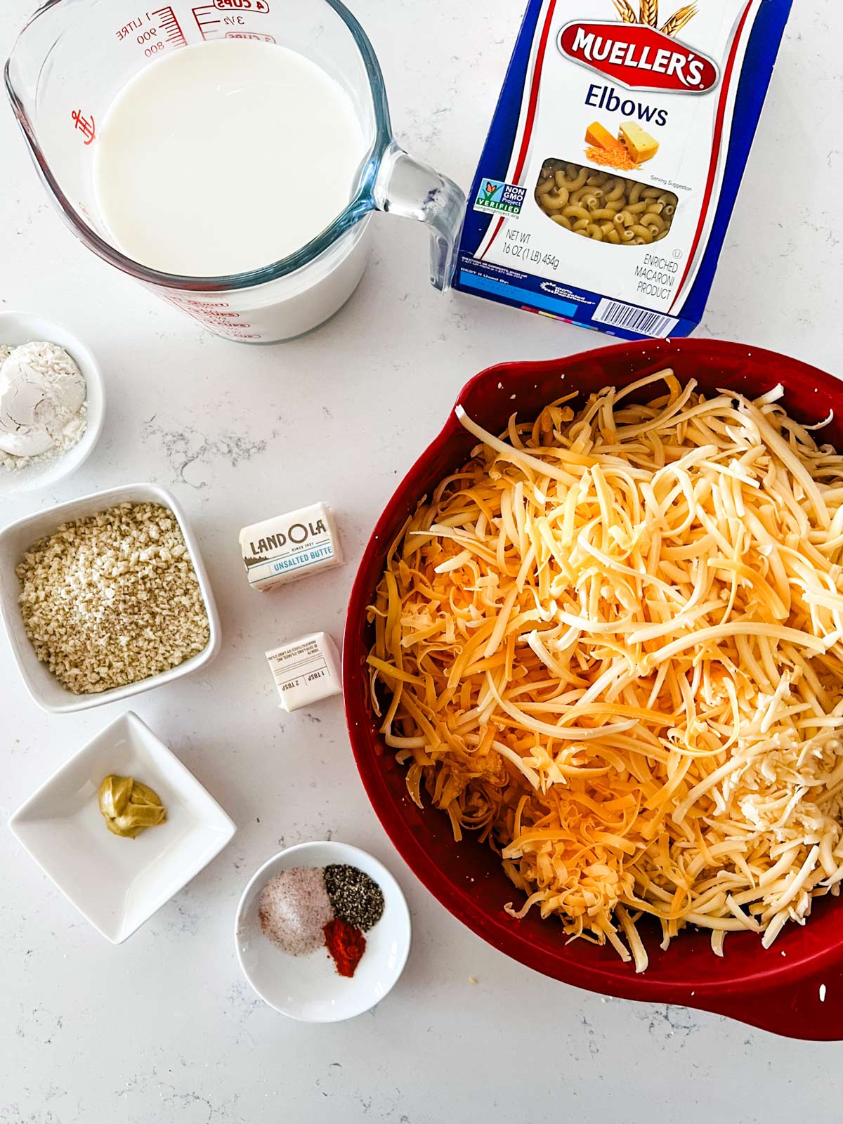 Overhead photo of milk, elbow noodles, shredded cheese, seasonings, butter, mustard, breadcrumbs, and flour.