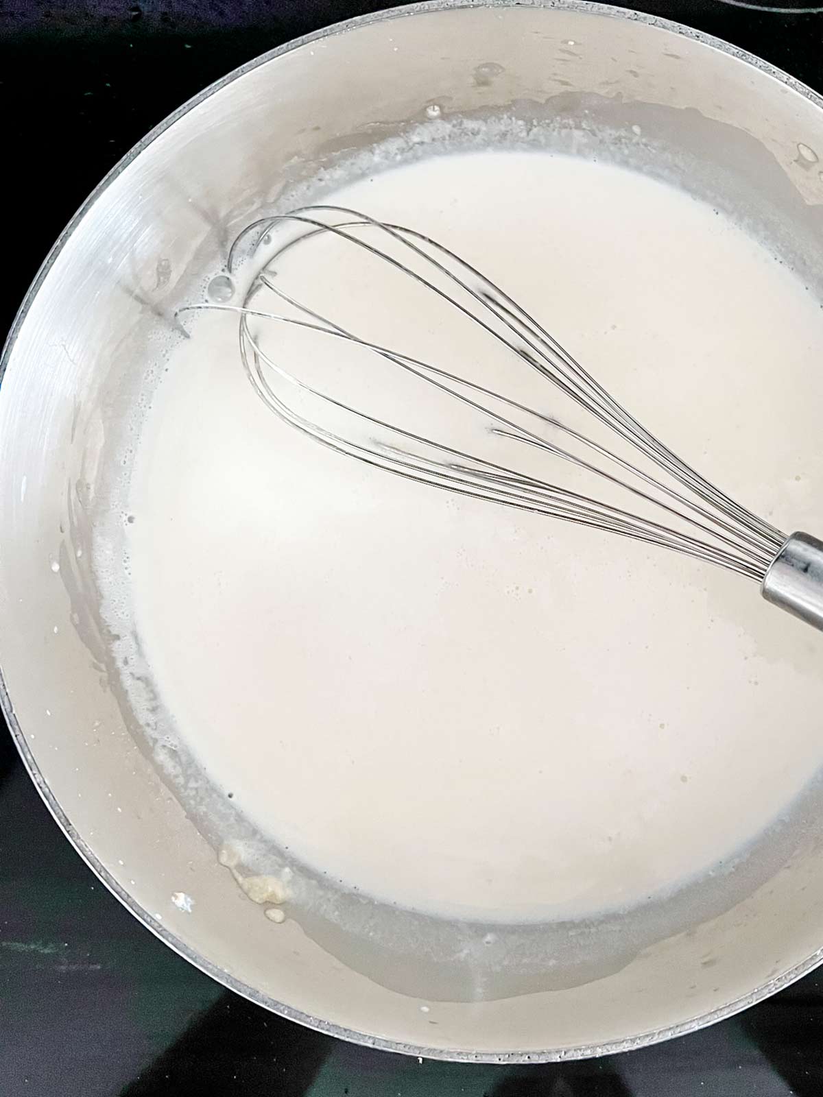 A cream sauce and whisk in a large pot.
