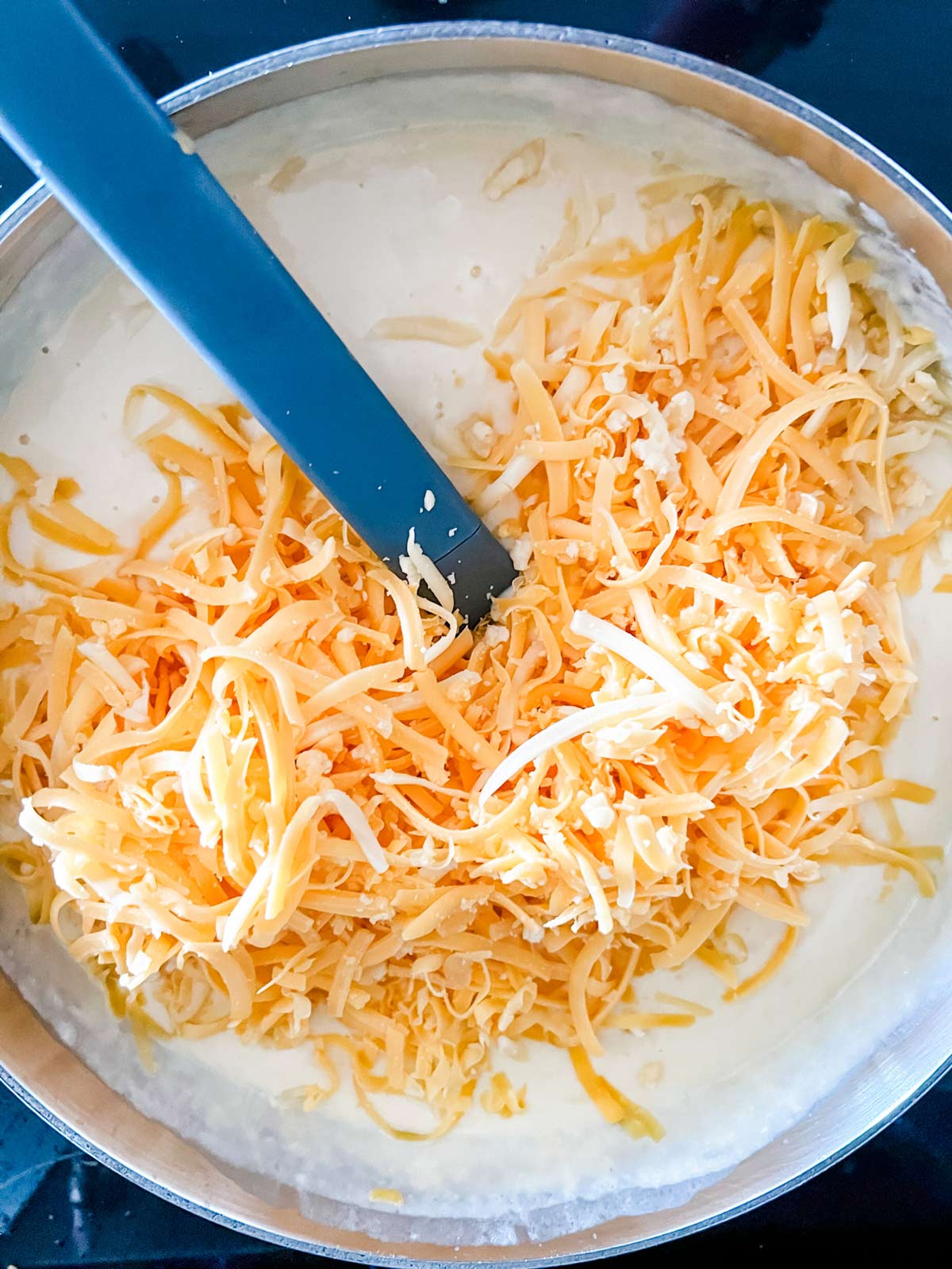 Shredded cheese being added to a cream sauce.