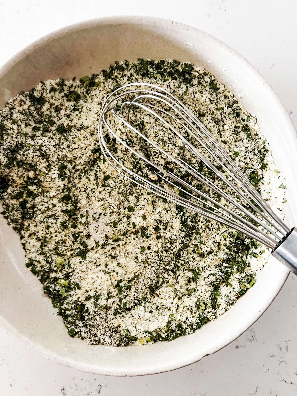 Dried buttermilk powder, crushed dried parsley leaves, dried chives, garlic powder, onion powder, mustard powder, dried dill, sugar, sea salt, and freshly ground black pepper being whisked together in a bowl.