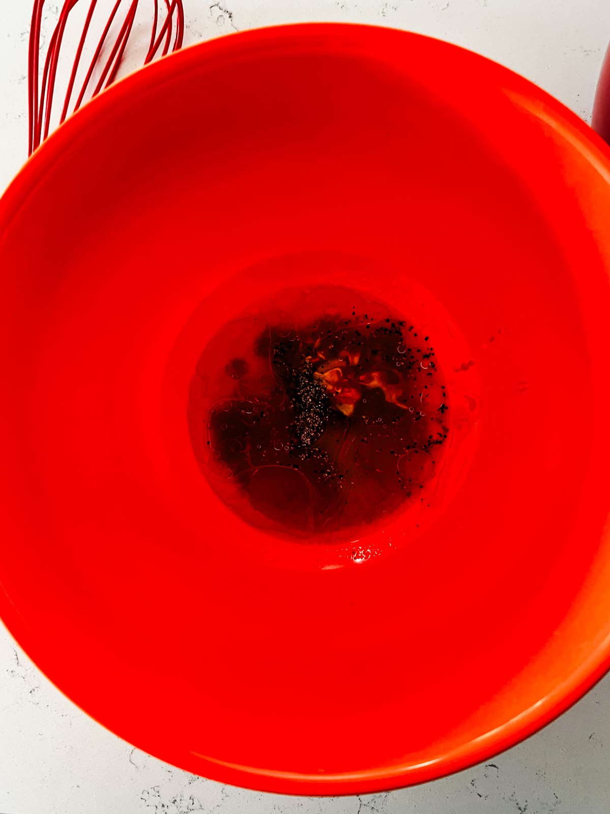 Oil, seasonings, honey, and sriracha in an orange bowl.