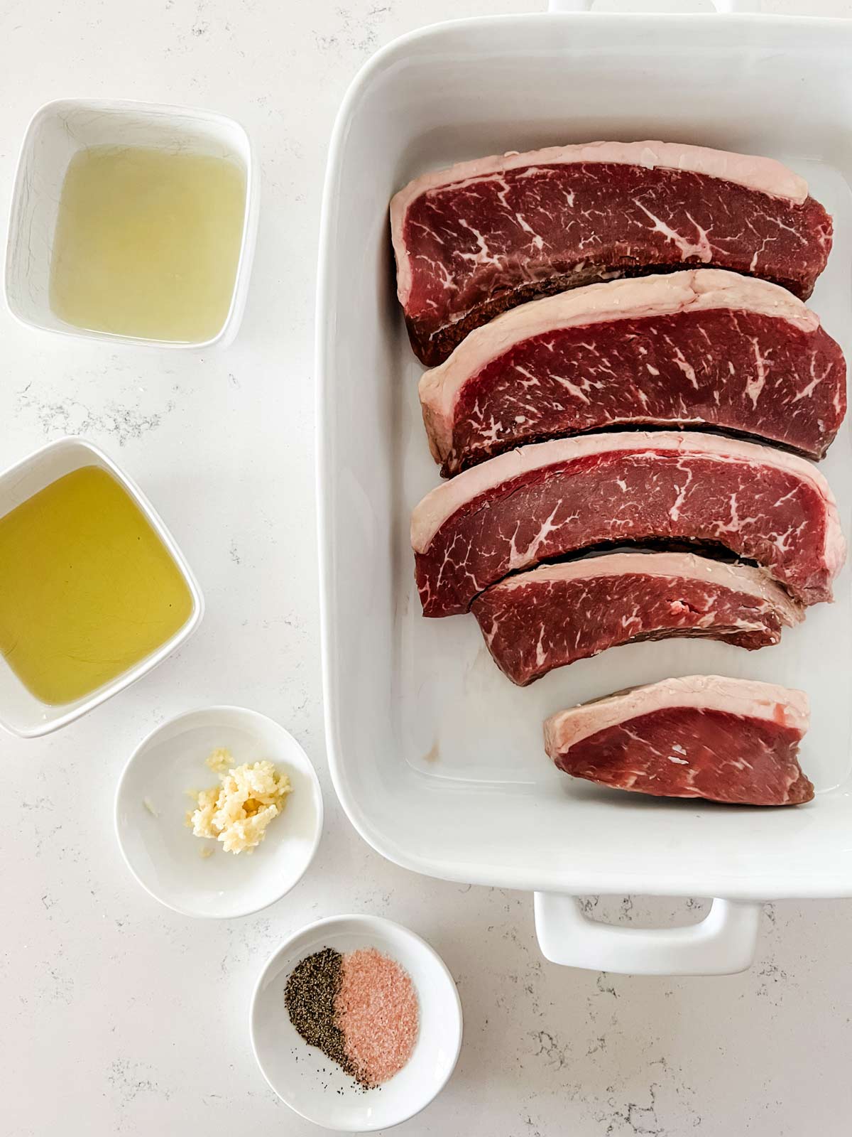 Overhead photo of picanha steaks, oil, lemon juice, garlic, and seasonings.