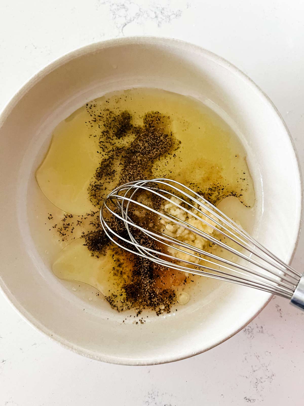 Avocado oil, lemon juice, garlic, salt, and pepper being whisked together in a bowl.