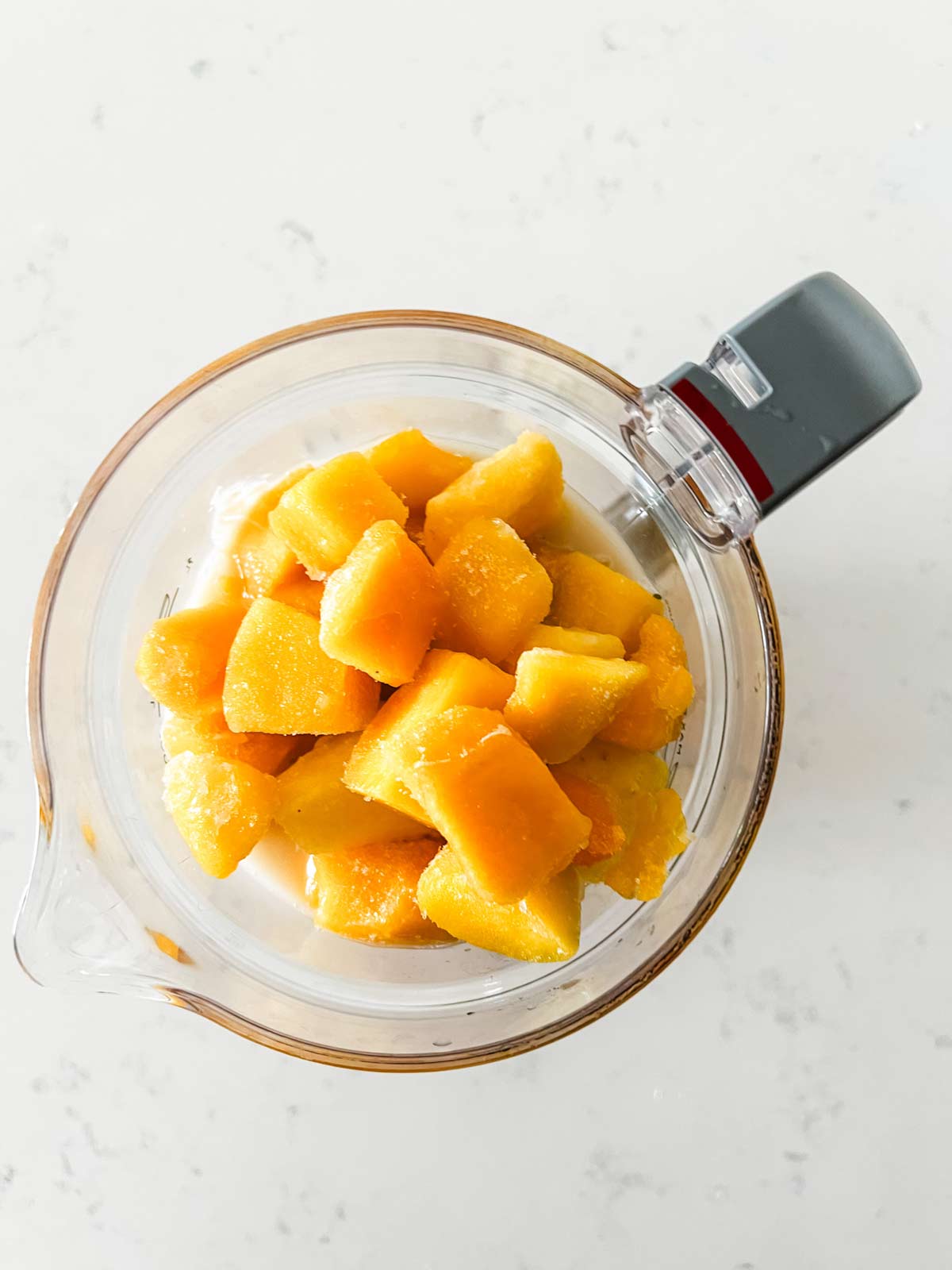 Overhead photo of pineapple mango smoothie ingredients in a blender.