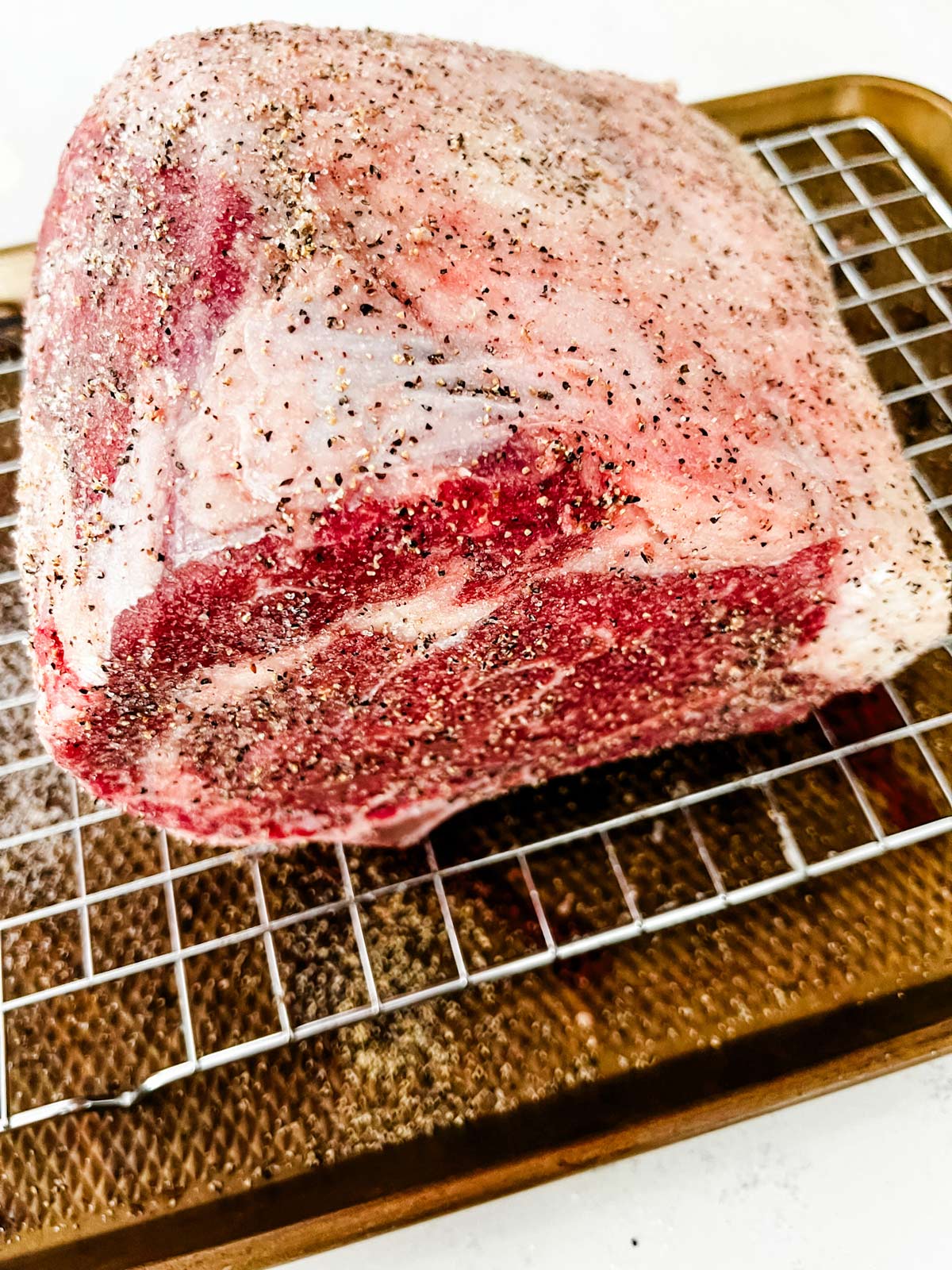 Prime rib roast that has been seasoned on a rack sitting on a baking sheet.