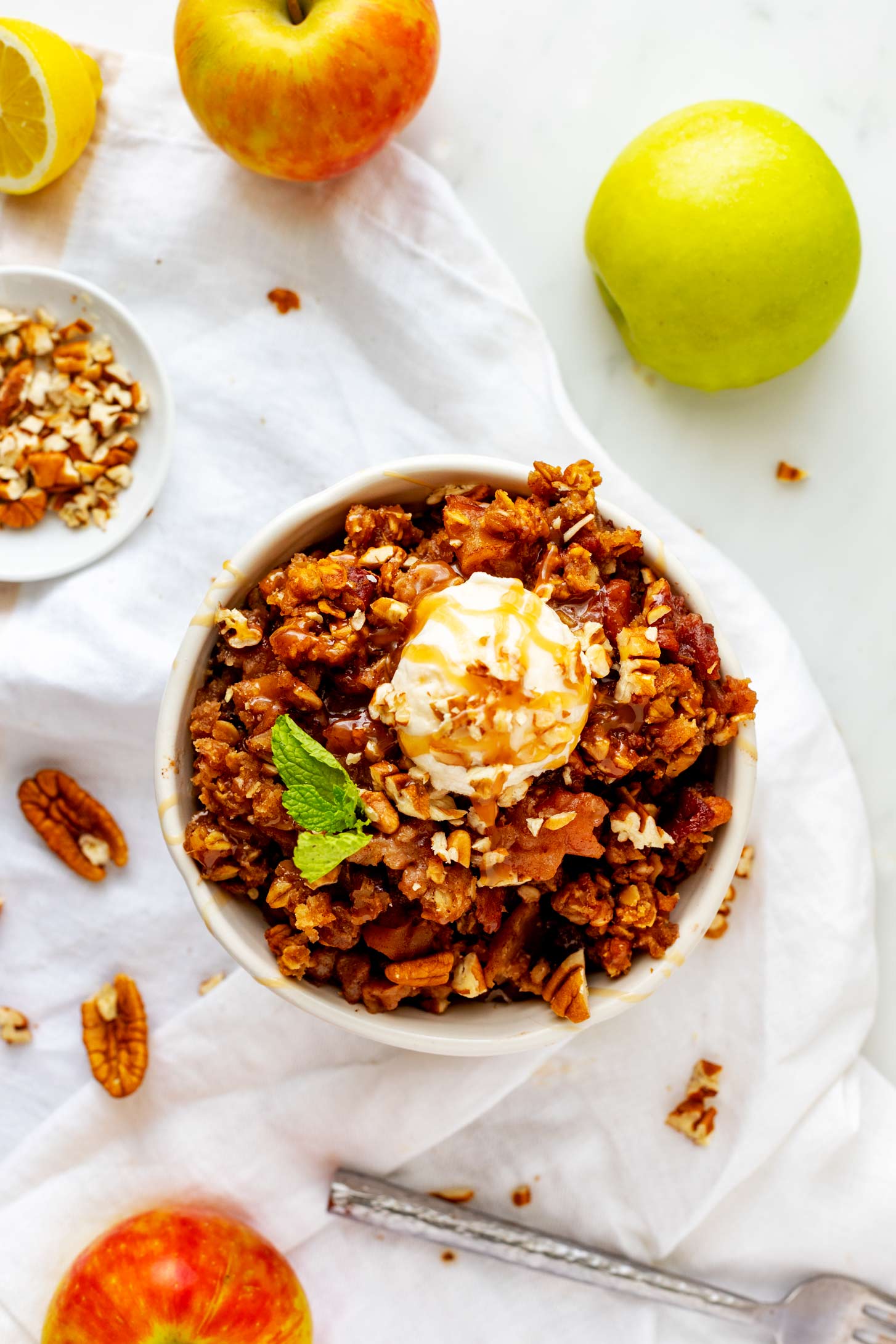 Overhead photo of slow cooker apple crisp in a bowl with ice cream, caramel sauce, and pecans.
