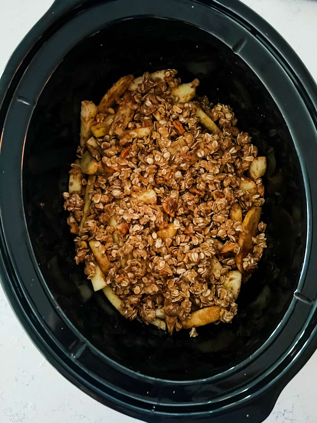 Overhead photo of an apple crisp in a slow cooker ready to cook.