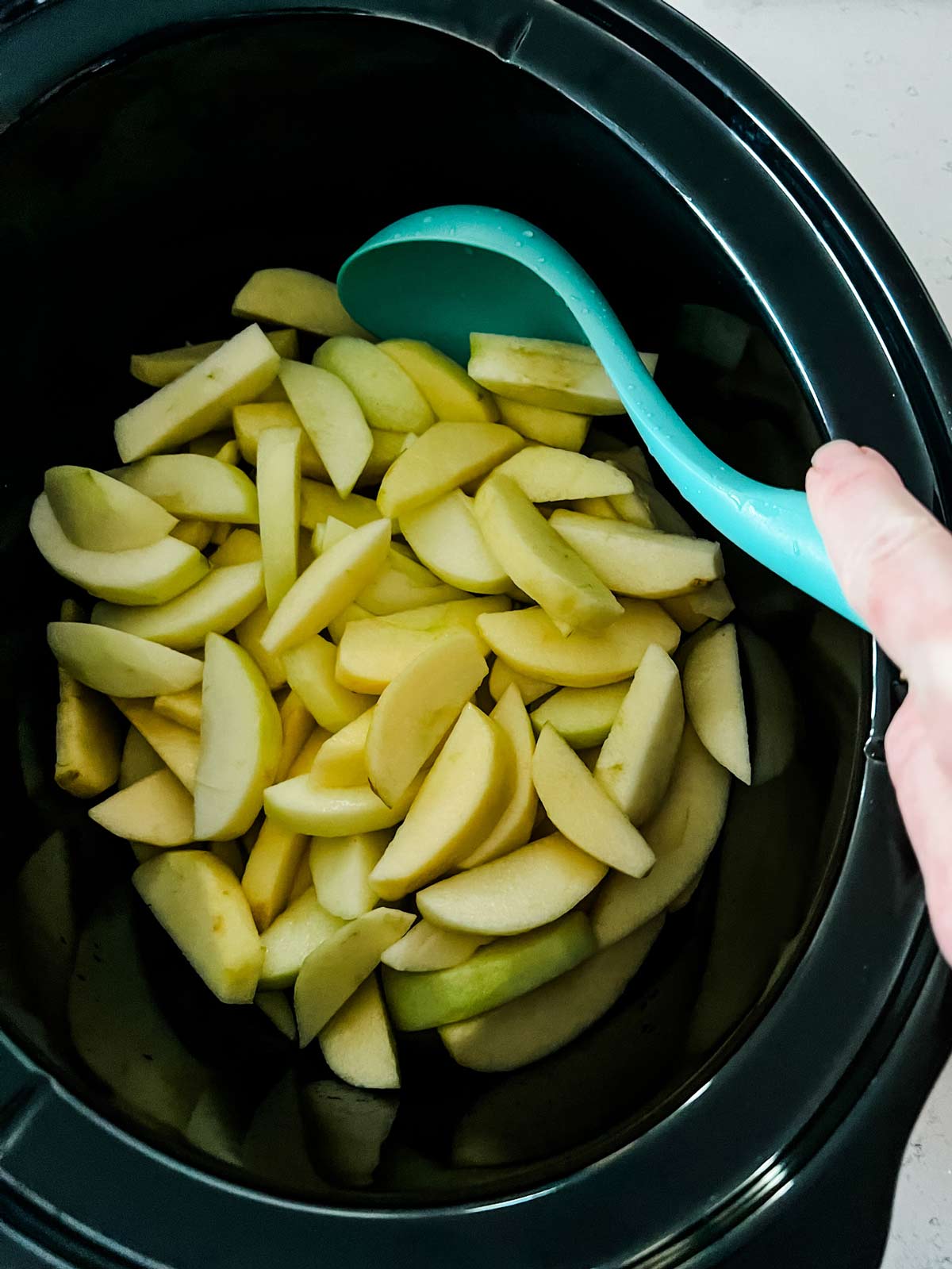Peeled and sliced apples being tossed with lemon juice in a slow cooker.