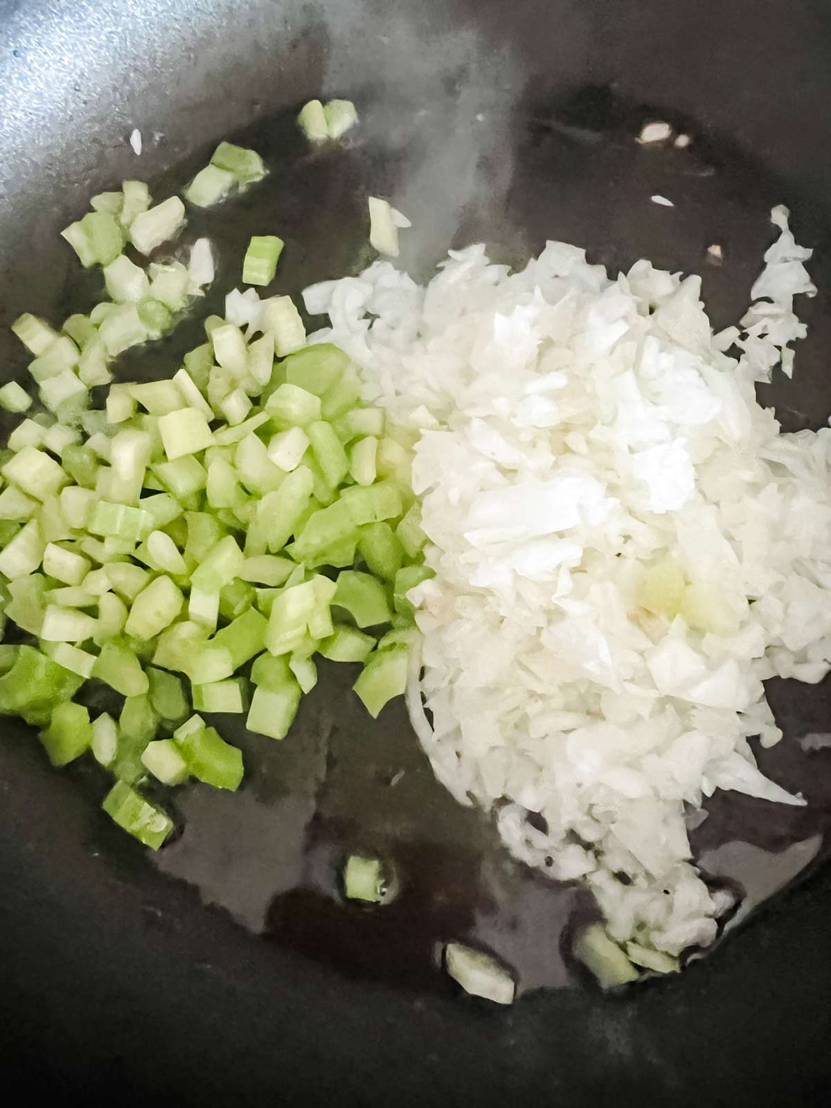 Onion and celery cooking in oil in a skillet.