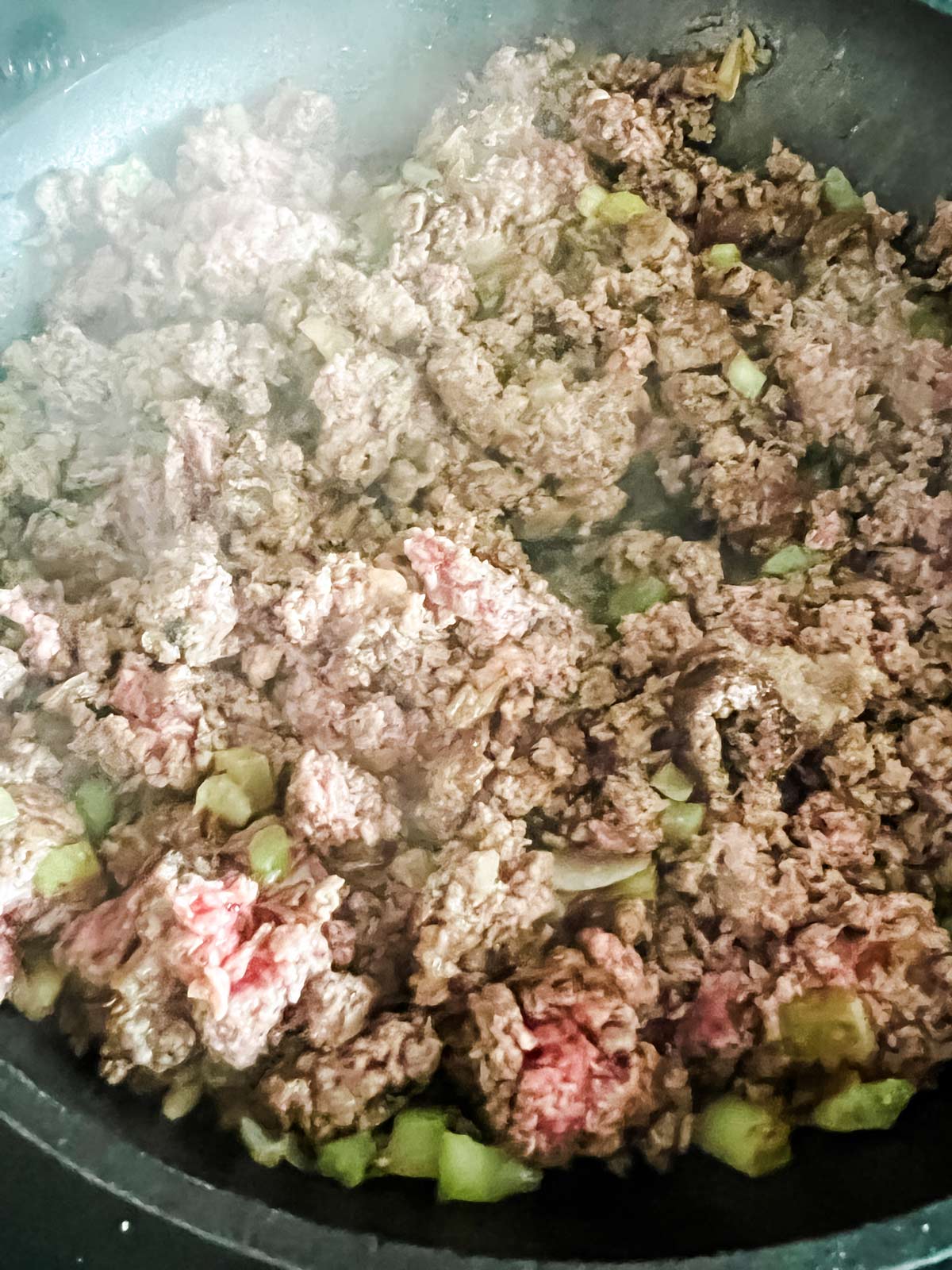 Ground beef being browned with onion and celery in a skillet.