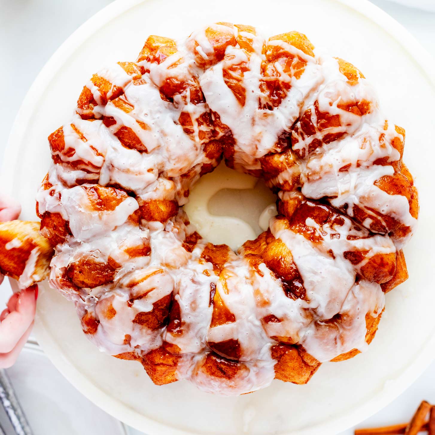 Overhead square photo of a bread machine monkey bread on a cake stand with a bite being pulled from it.